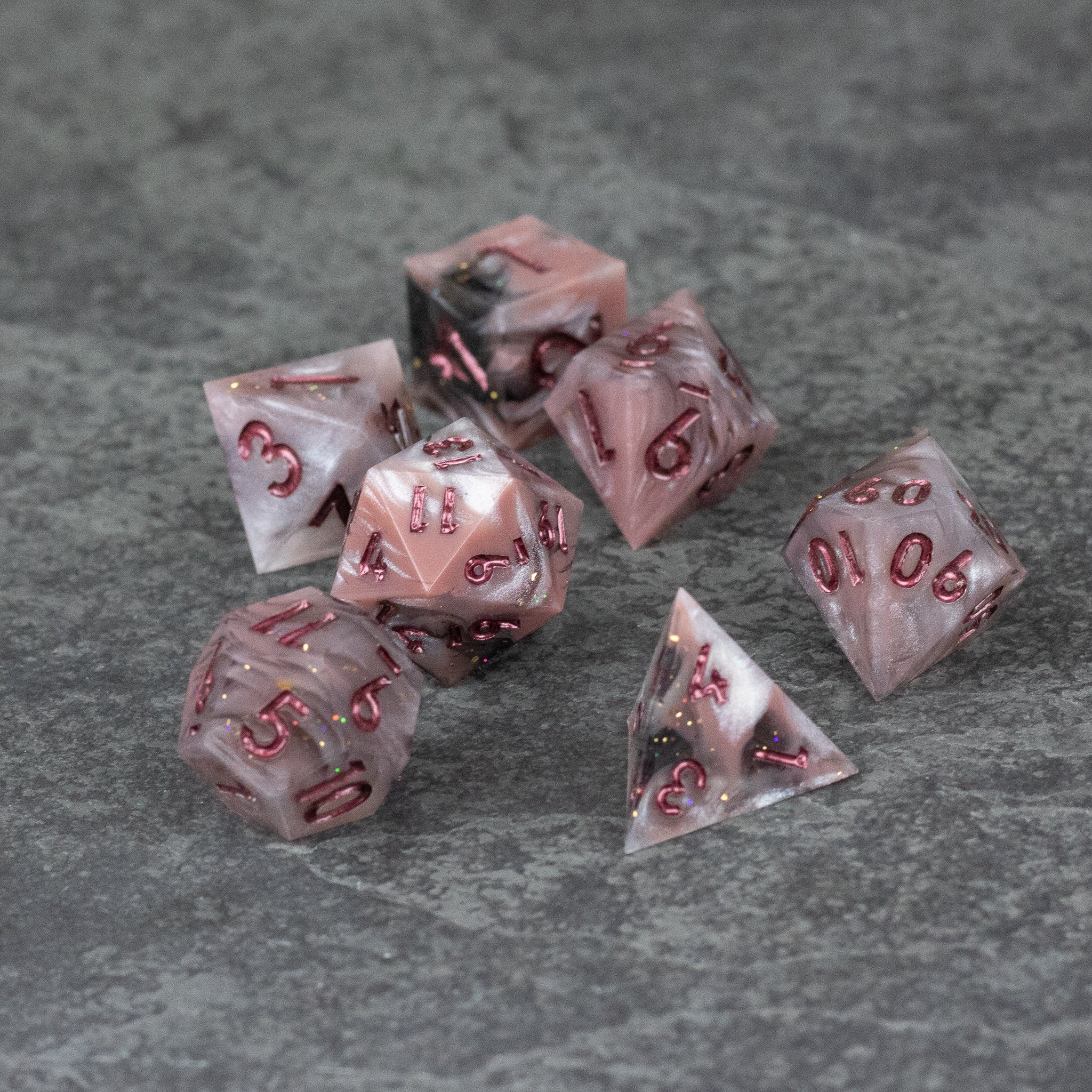 Rosestone Dice Set - Set of seven translucent red and white marbled polyhedral dice with sharp edges and red numbers on a gray textured surface.
