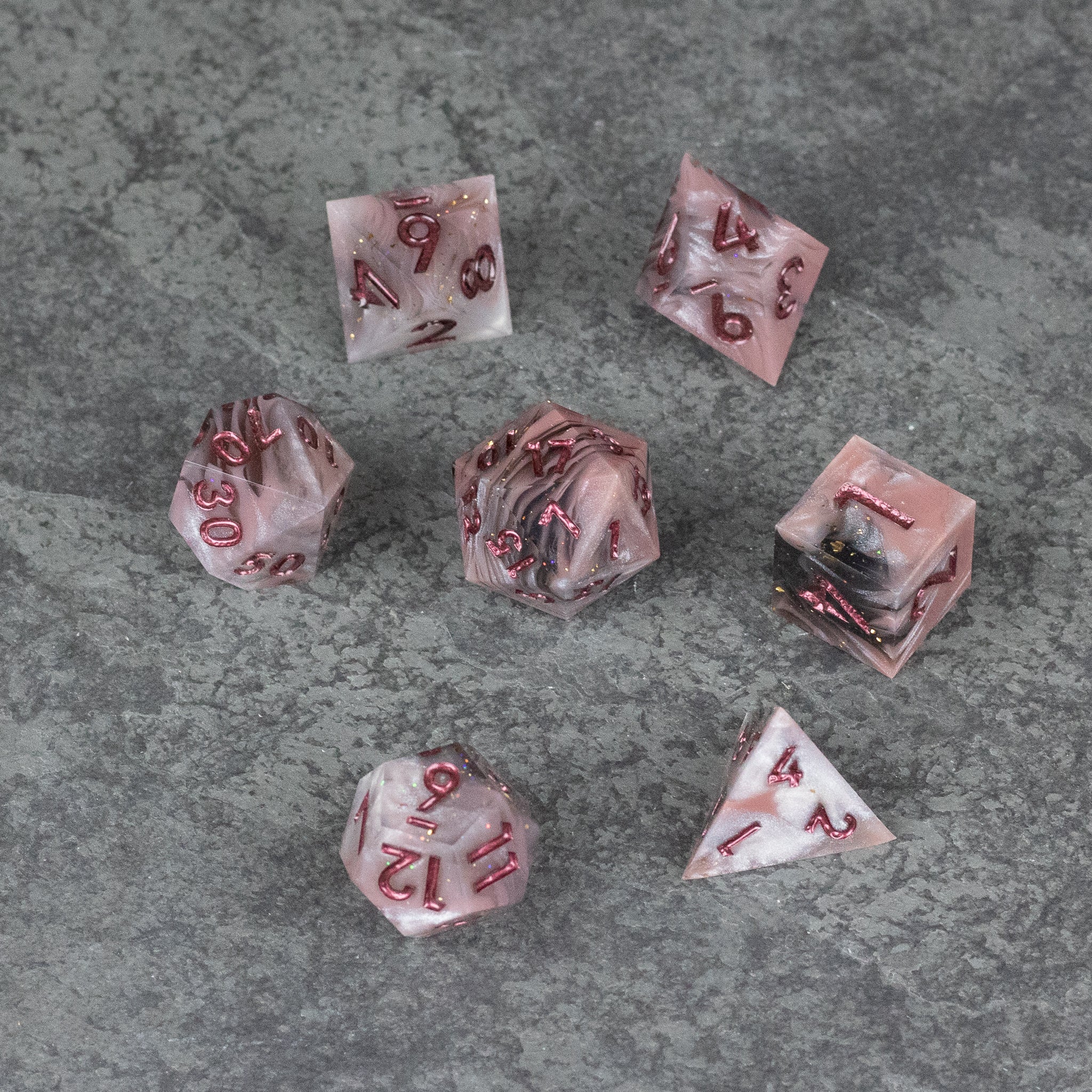 Rosestone Dice Set - Seven red and white marbled polyhedral dice with sharp edges, including D4, D6, D8, D10, percentile, D12, and D20, on a gray