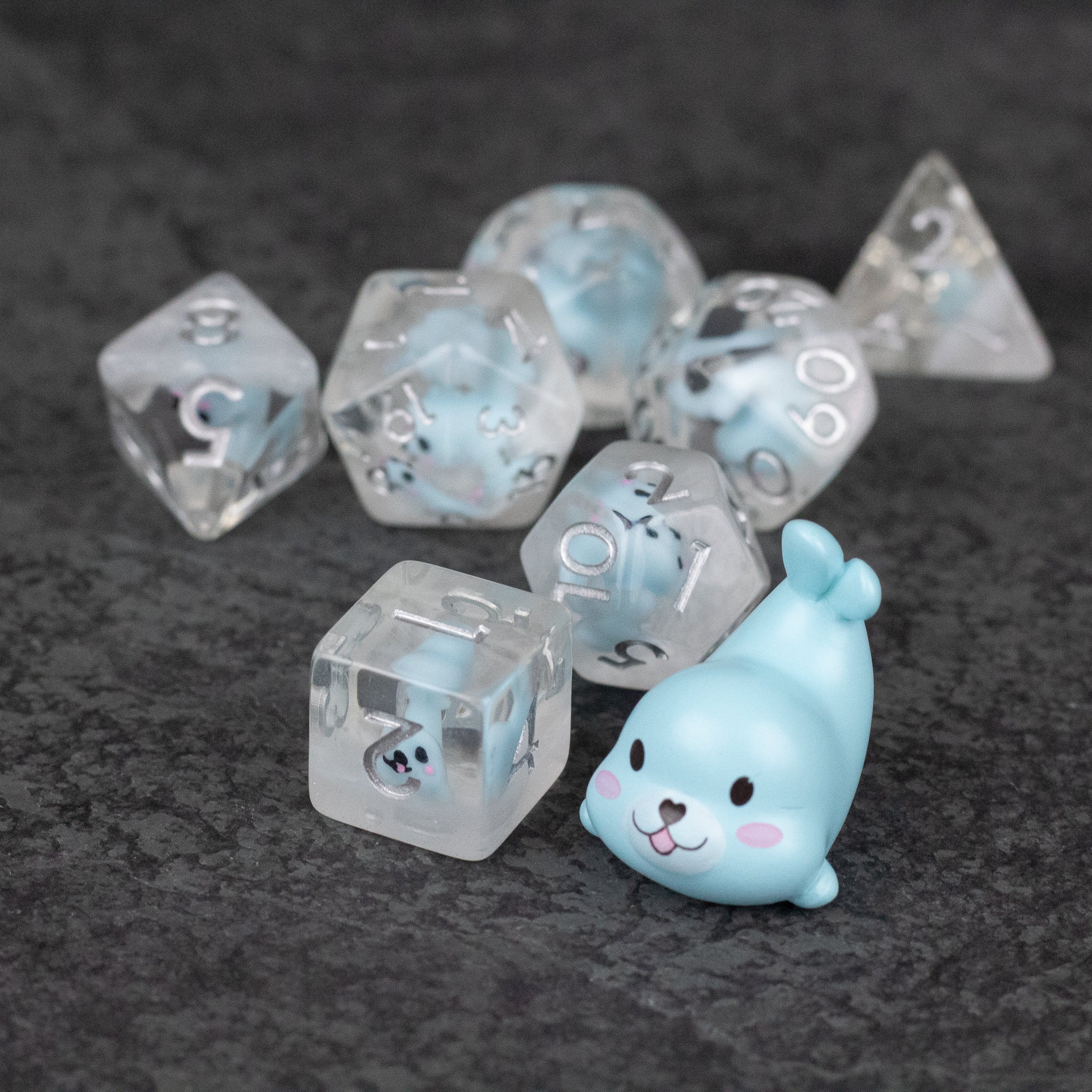 Blue Seal Dice Set - Translucent blue and clear polyhedral dice with white numbers and a small blue seal figurine on dark textured surface.