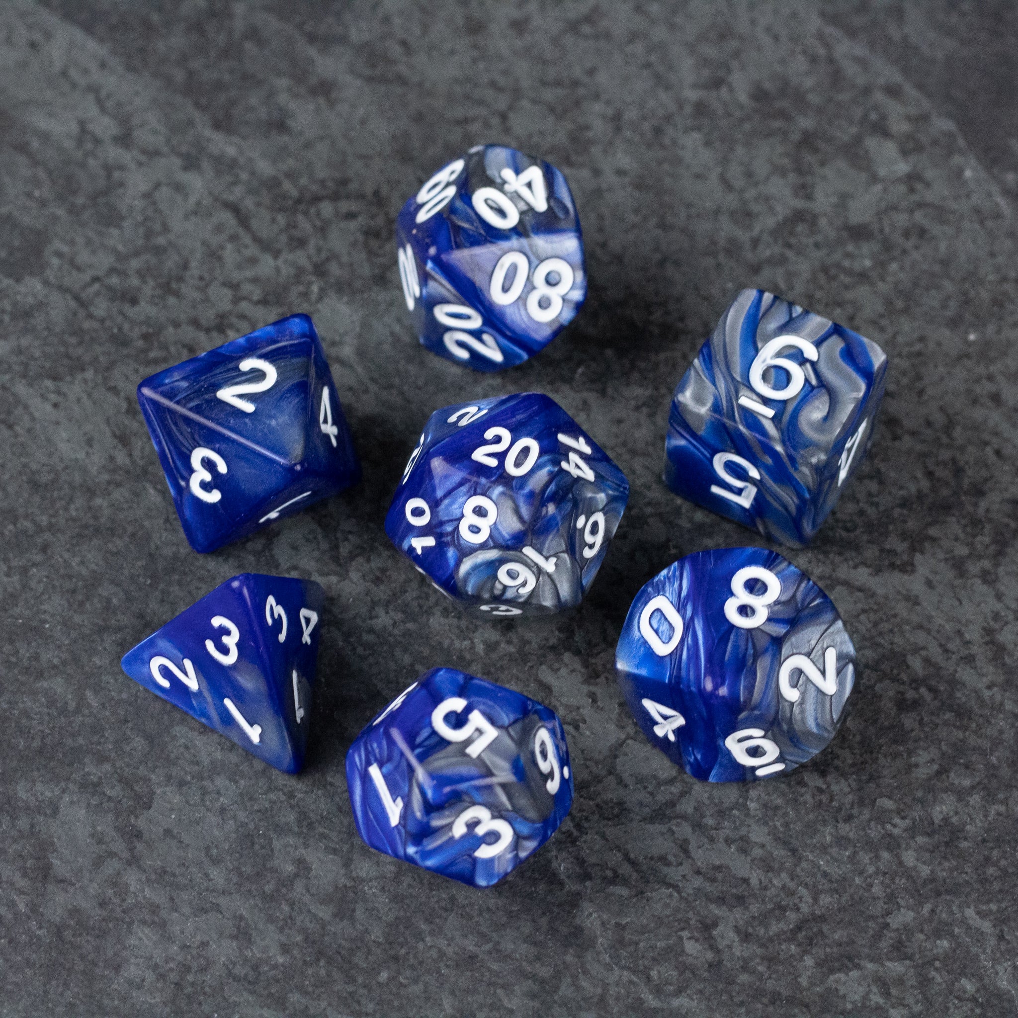 Royal Blue and Silver Acrylic Dice Set - Set of seven royal blue acrylic dice with white numbers, including d4, d6, d8, d10, d12, and d20, on dark textured surface.