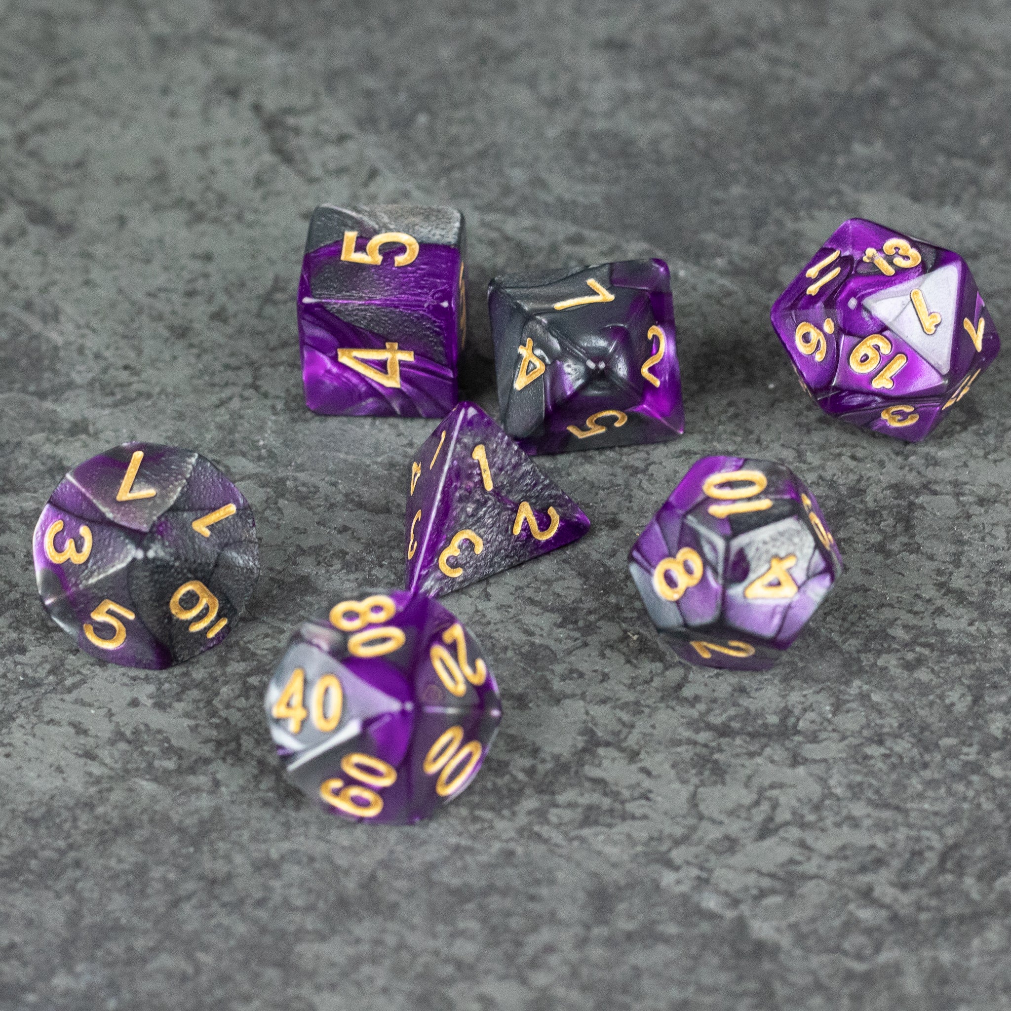 Purple and Black Marbled Dice Set - Seven purple and black marbled acrylic dice set with gold numbers on gray textured background.