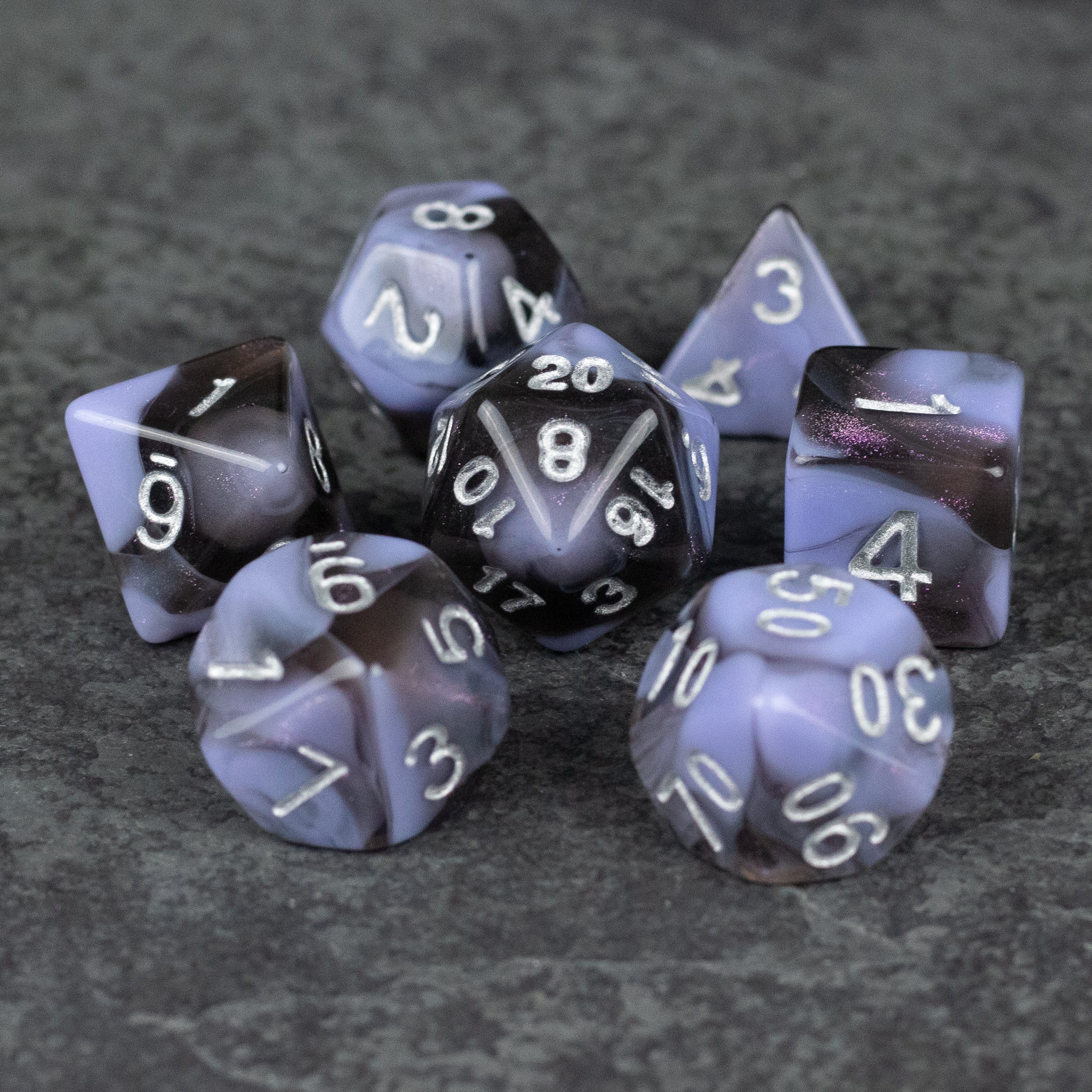 Periwinkle and Black Marbled Dice Set - Set of seven acrylic dice with marbled periwinkle and black coloring and white numbers on a dark textured surface.