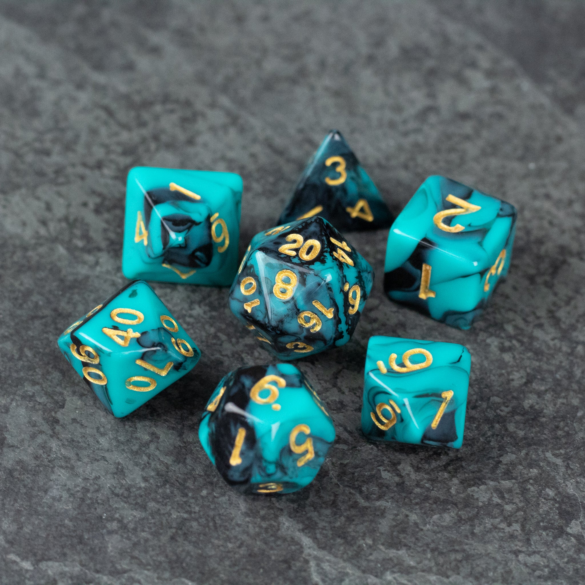 Mint and Black Marbled Dice Set - Set of seven acrylic dice with mint and black marbled pattern and gold numbers on gray surface.