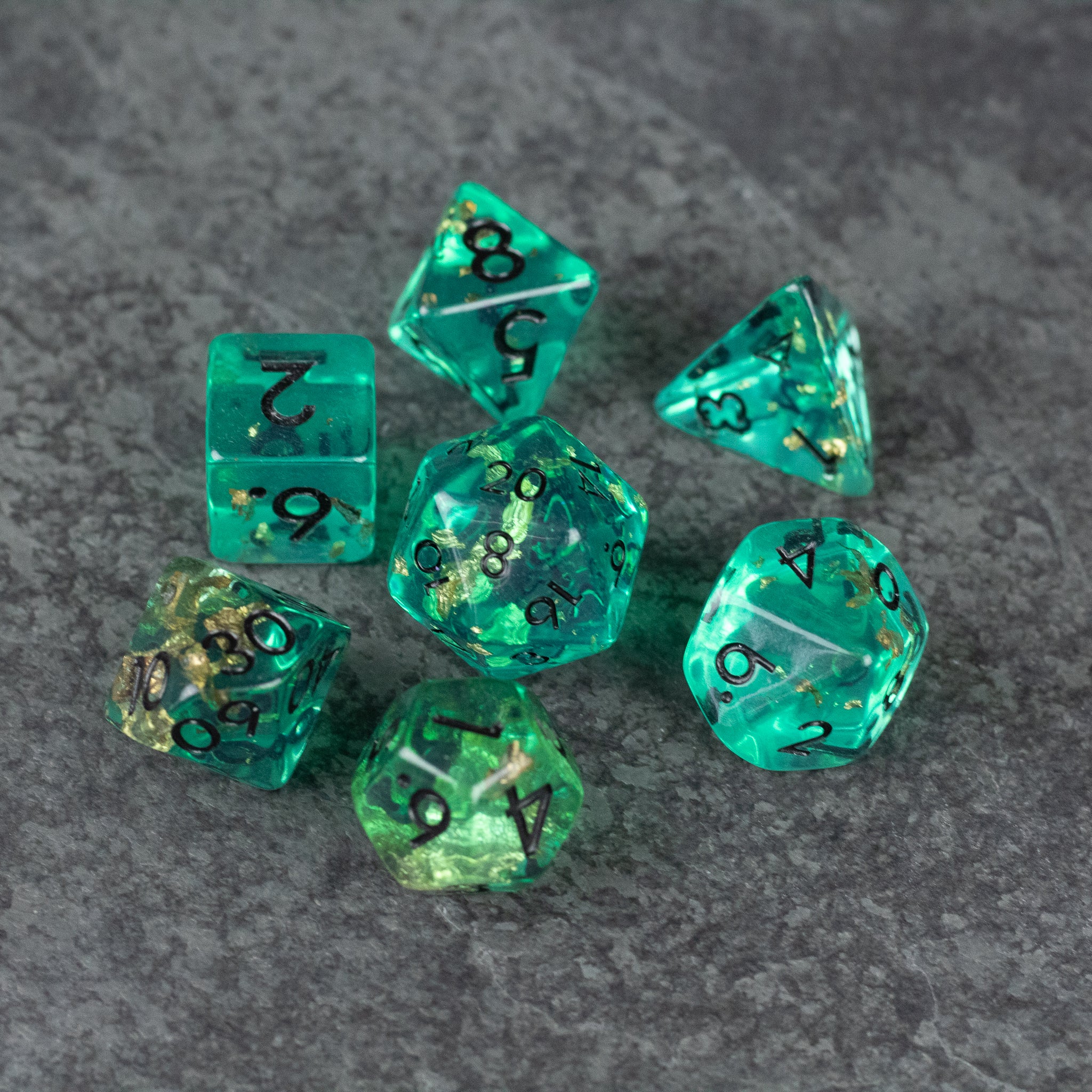 Teal Foil Dice Set - Set of seven teal foil polyhedral dice with black numbering on gray textured surface.
