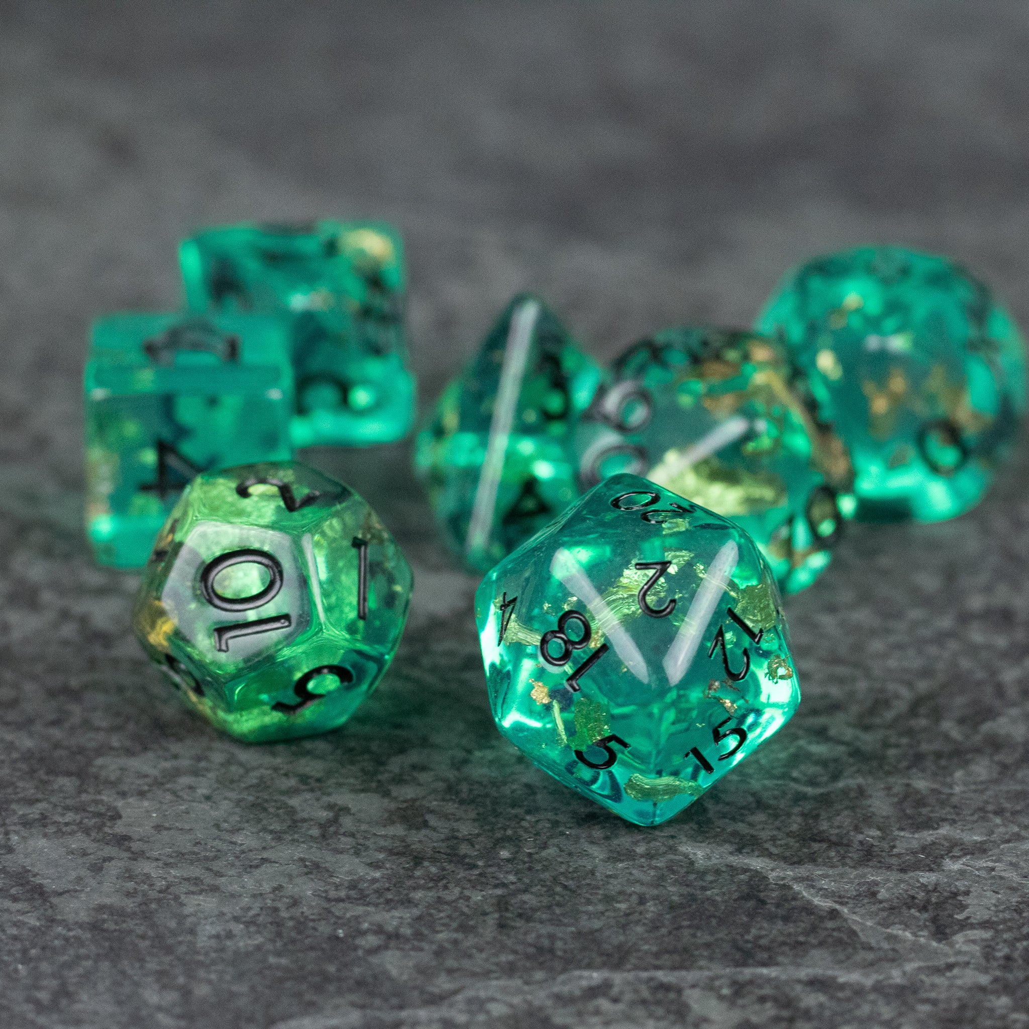 Teal Foil Dice Set - Teal translucent foil dice set with black numbers, including various polyhedral shapes on a gray surface.
