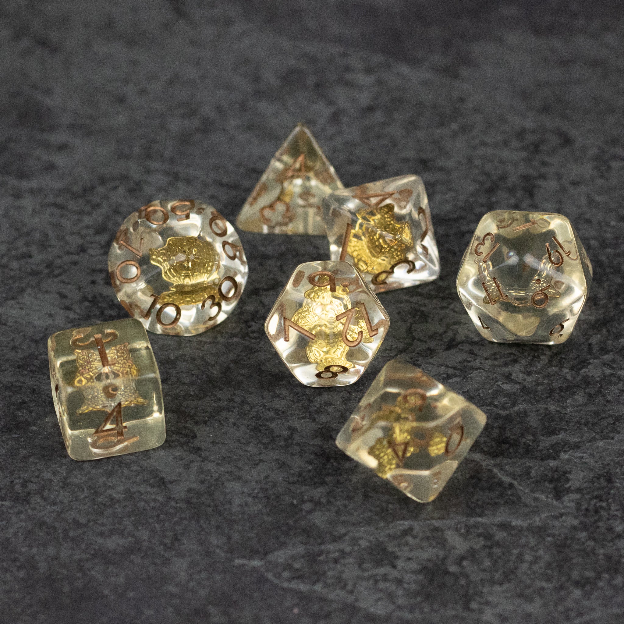 Gold Charm Butterfly Dice Set - Seven translucent dice with embedded gold butterfly charms, including a d20, d12, d10, d8, d6, and d4, on a dark surface.