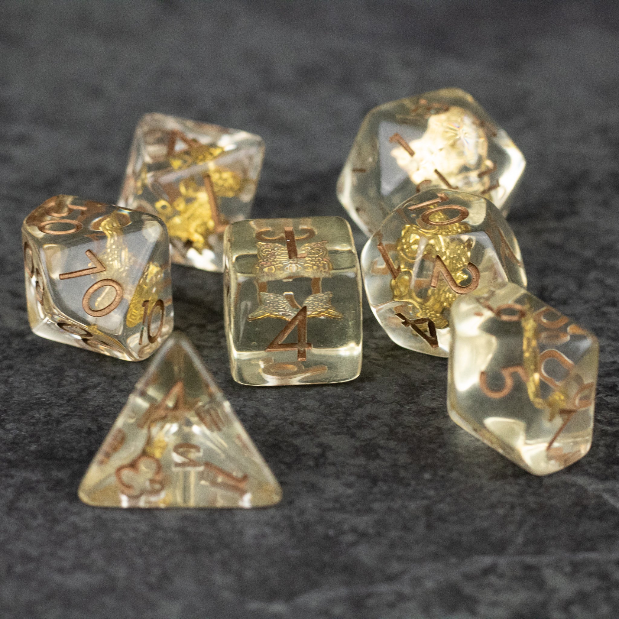 Gold Charm Butterfly Dice Set - Transparent dice set with gold butterfly charms and gold numbers on a dark surface.