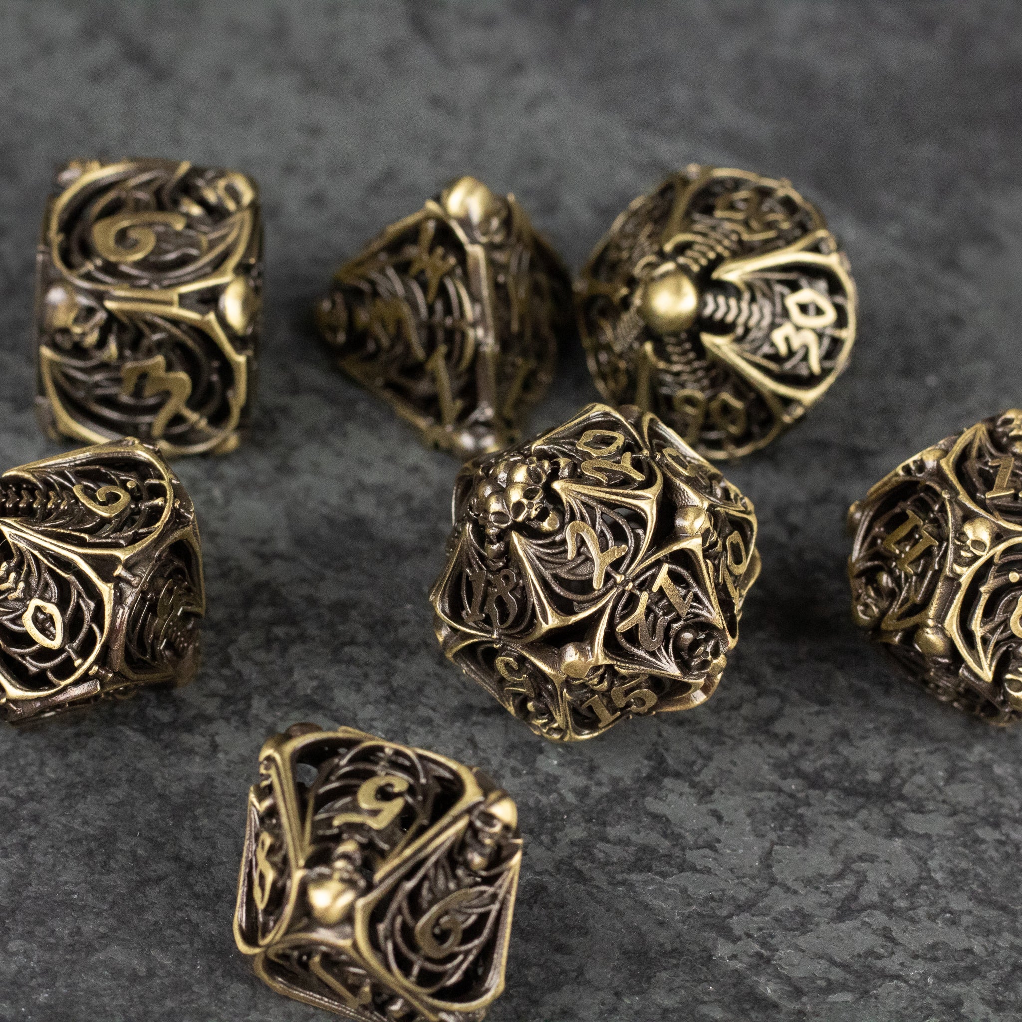 Bone Crypt Dice Set - Intricate metallic gold dice set with hollow, filigree bone and skull designs on a dark textured surface.