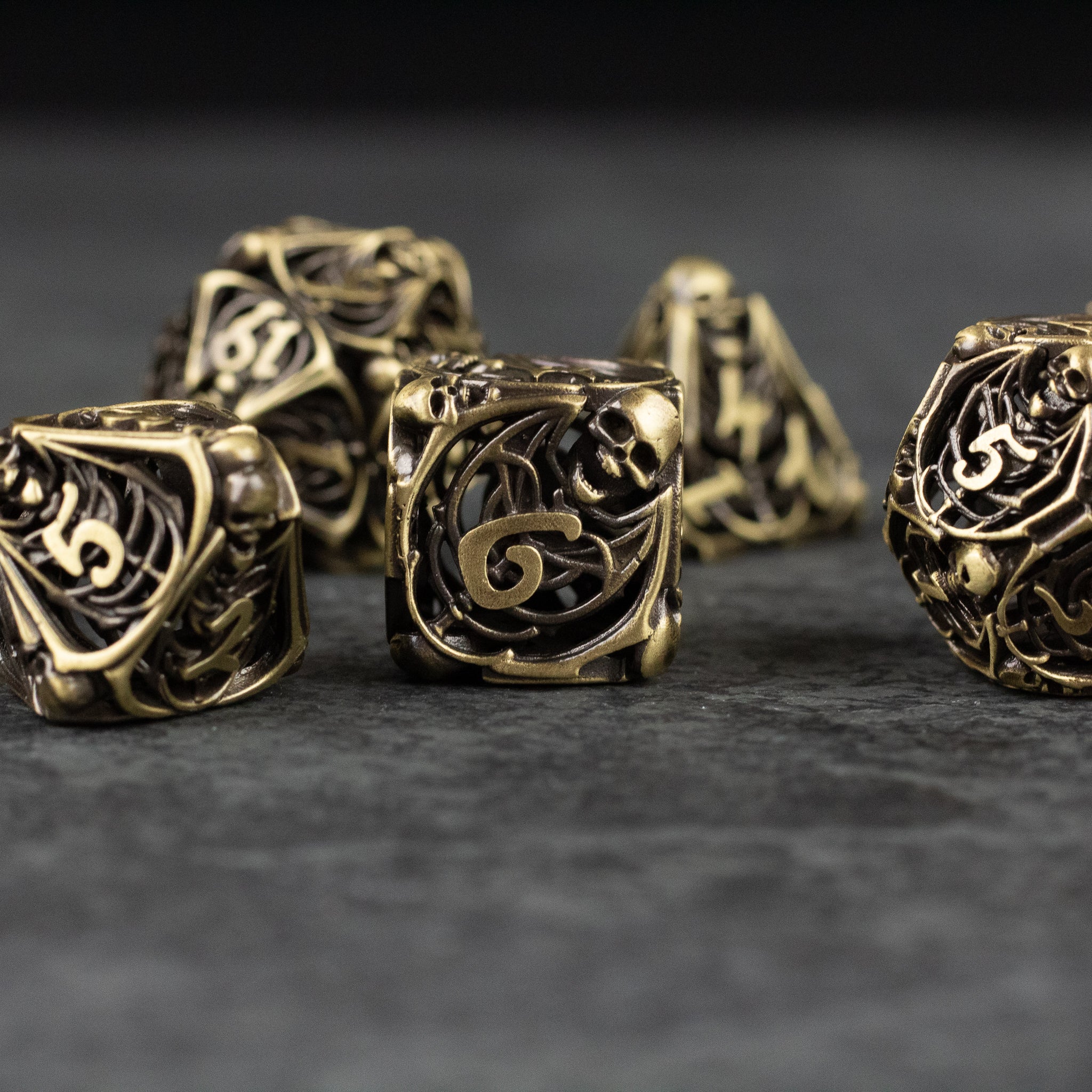 Bone Crypt Dice Set - Set of hollow metal dice with intricate bone-inspired skull and swirl engravings in antique gold finish.