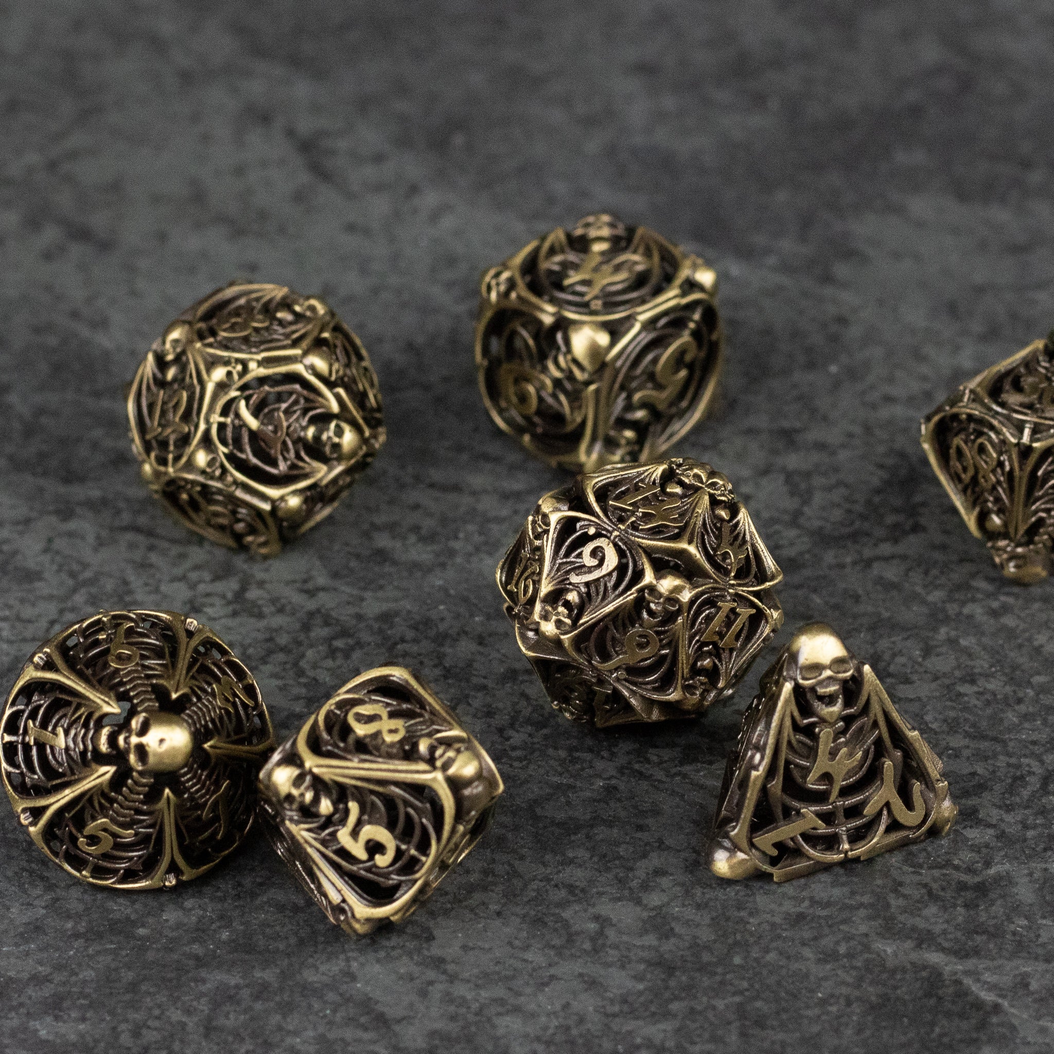 Bone Crypt Dice Set - Hollow metal dice set in antique gold with bone and skeletal designs, including d20, d12, d10, d8, d6, and d4 shapes.
