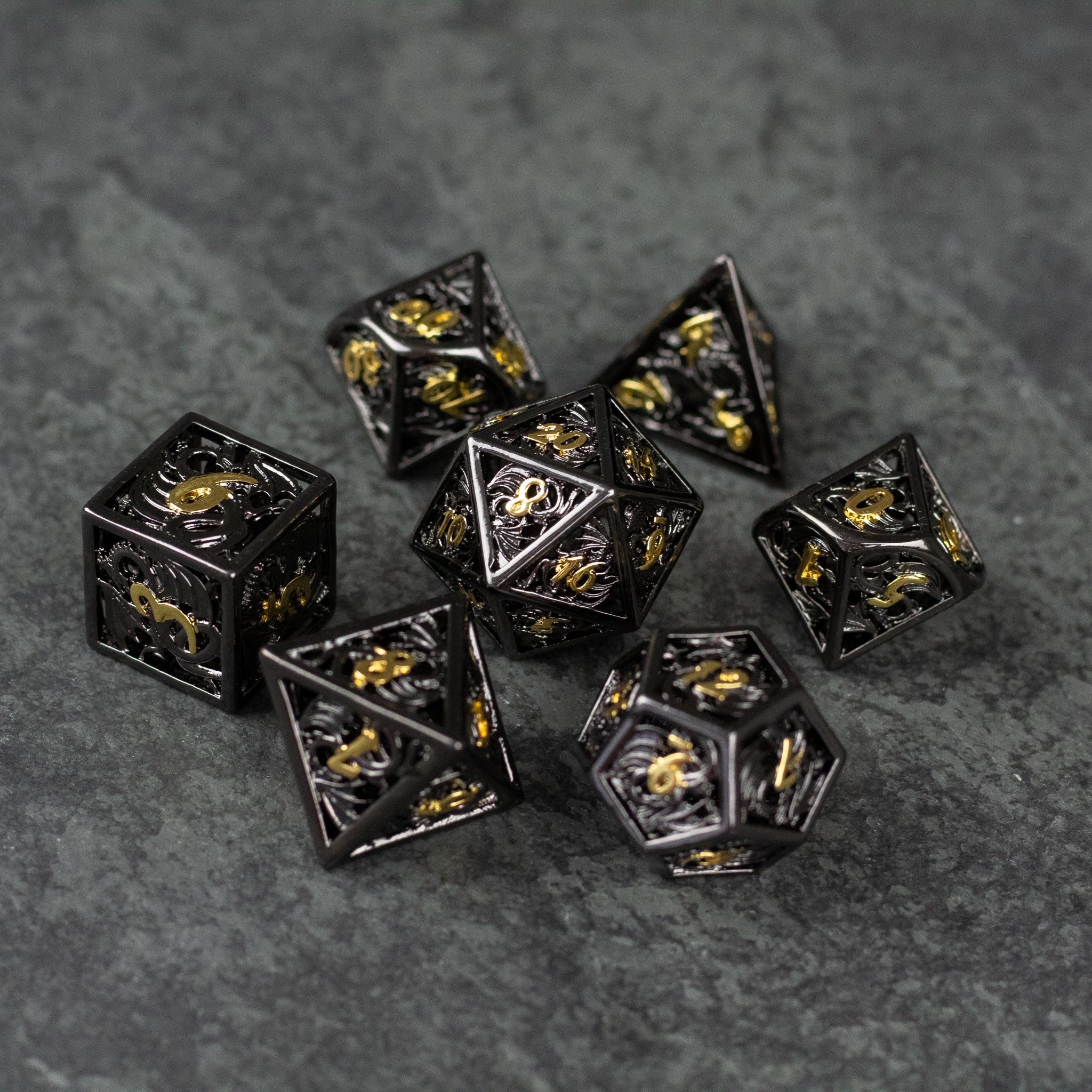 Black and Gold Dragon Hollow Dice Set - Black and gold hollow metal dice set featuring dragon designs on a dark textured surface.