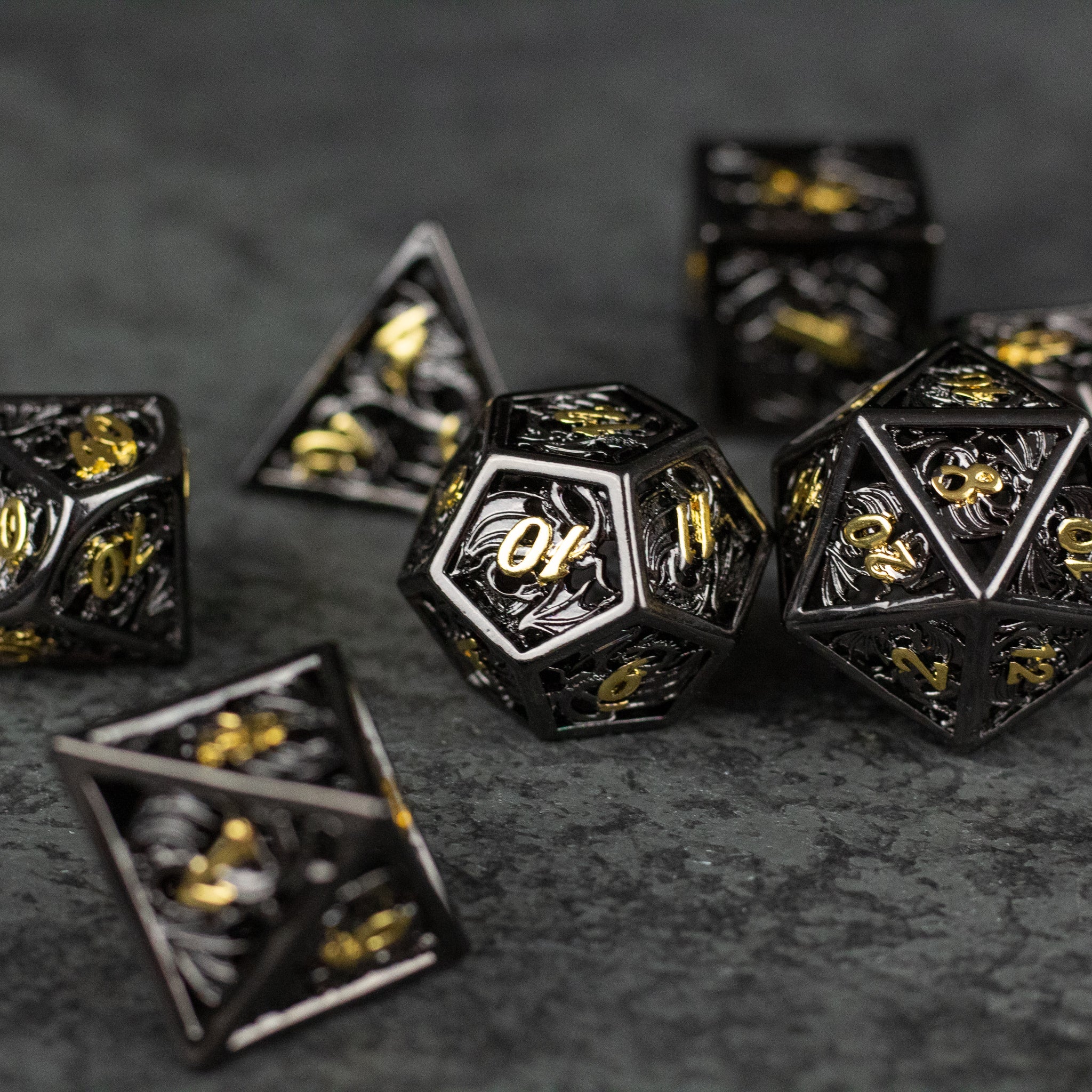 Black and Gold Dragon Hollow Dice Set - Black and gold metal hollow polyhedral dice set with dragon-themed engravings on dark surface.