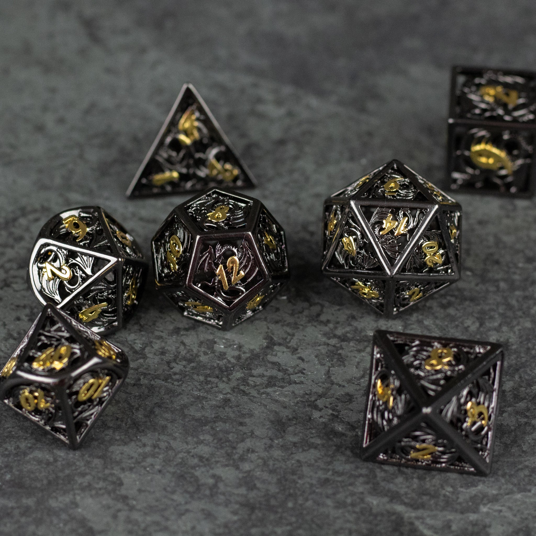 Black and Gold Dragon Hollow Dice Set - Black and gold hollow metal polyhedral dice set with dragon designs on a dark surface.
