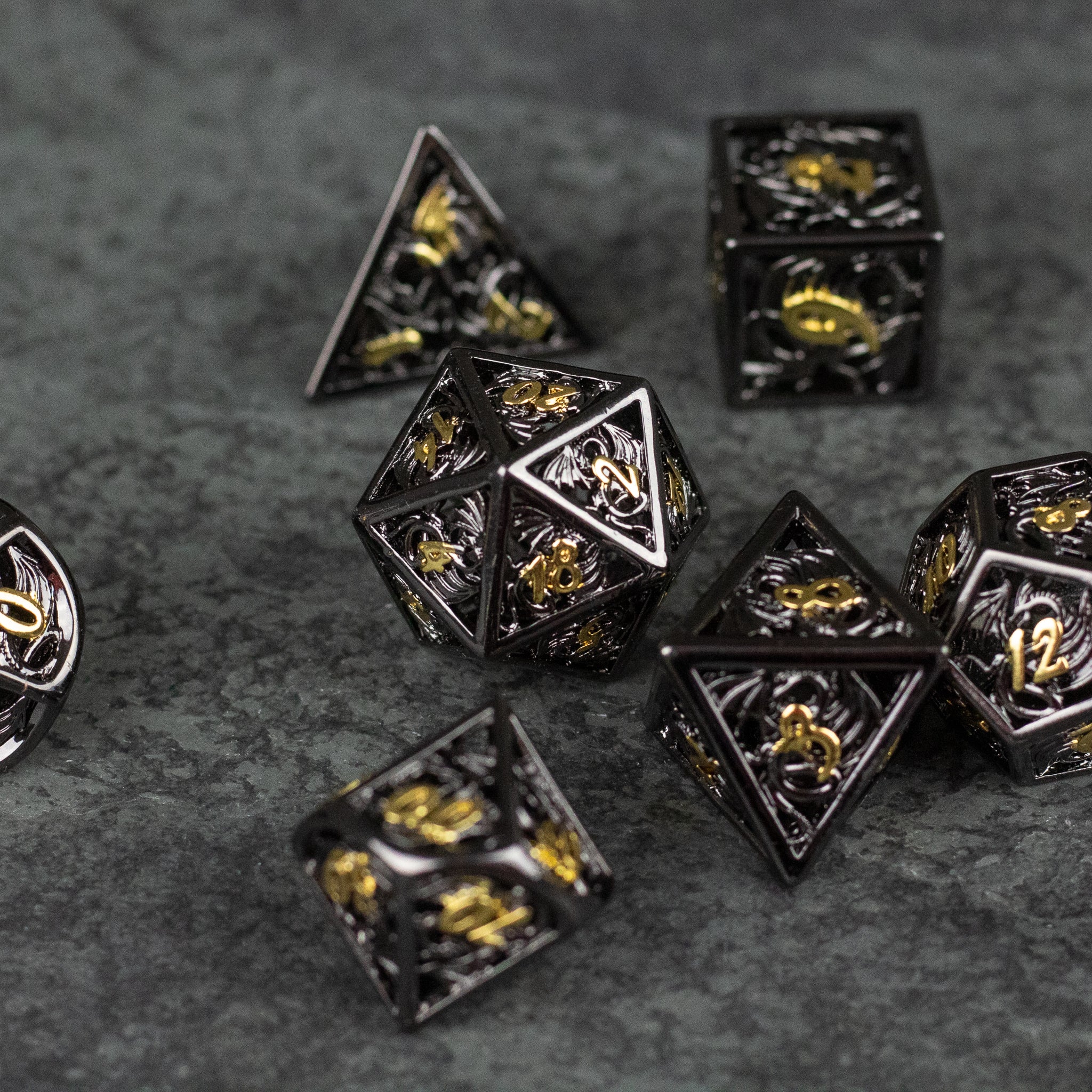 Black and Gold Dragon Hollow Dice Set - Black and gold metal hollow dice set with dragon engravings, including polyhedral shapes.