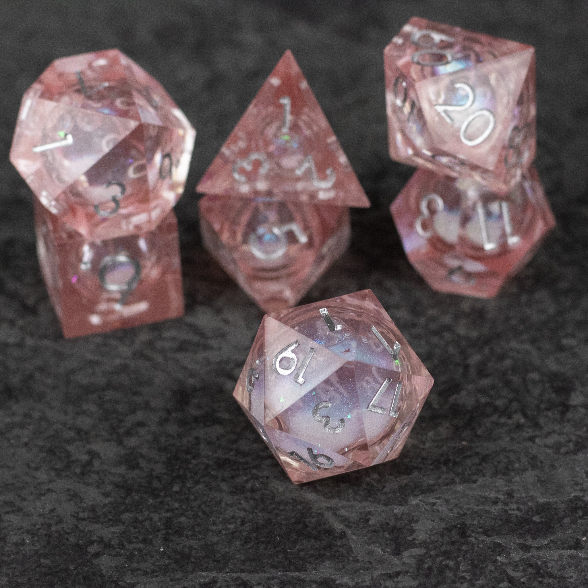 Fairy Dust - Liquid Core Dice Set - Transparent pink liquid core sharp-edged dice set with white numbers on dark background.