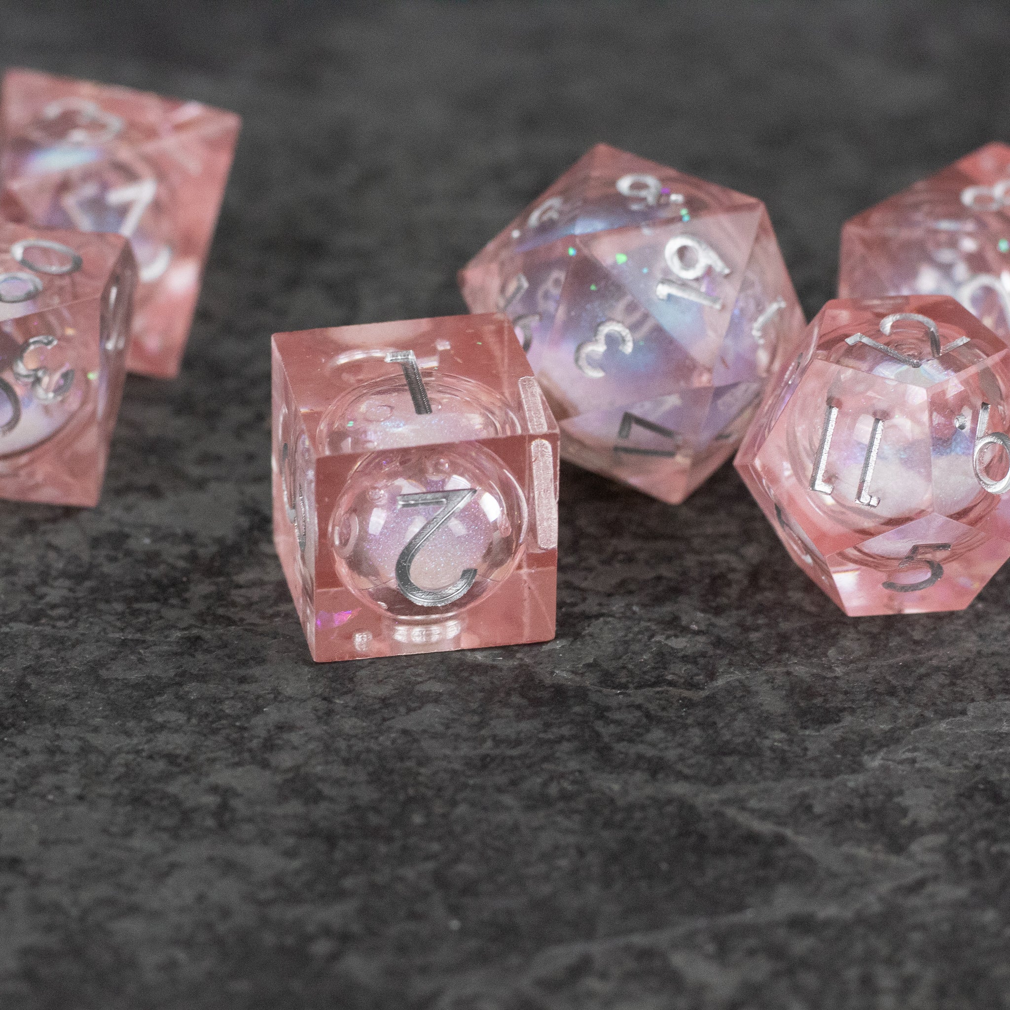 Fairy Dust - Liquid Core Dice Set - Set of translucent pink polyhedral dice with liquid core and sharp edges, featuring white numbering.