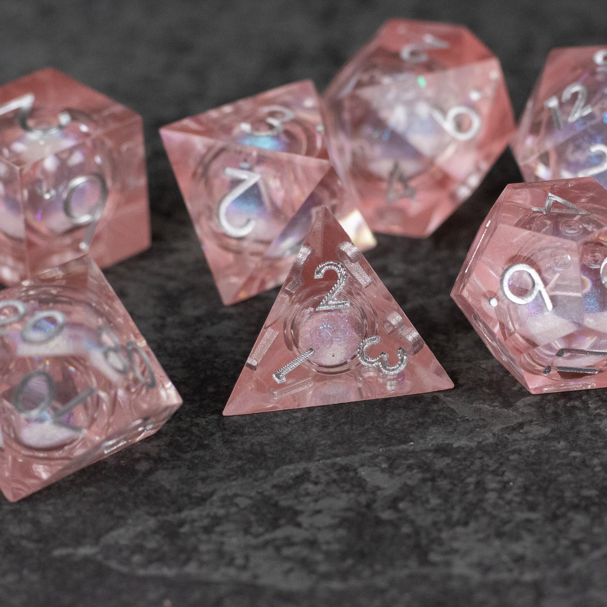 Fairy Dust - Liquid Core Dice Set - Set of seven translucent pink sharp-edged polyhedral dice with liquid core and silver numbering.