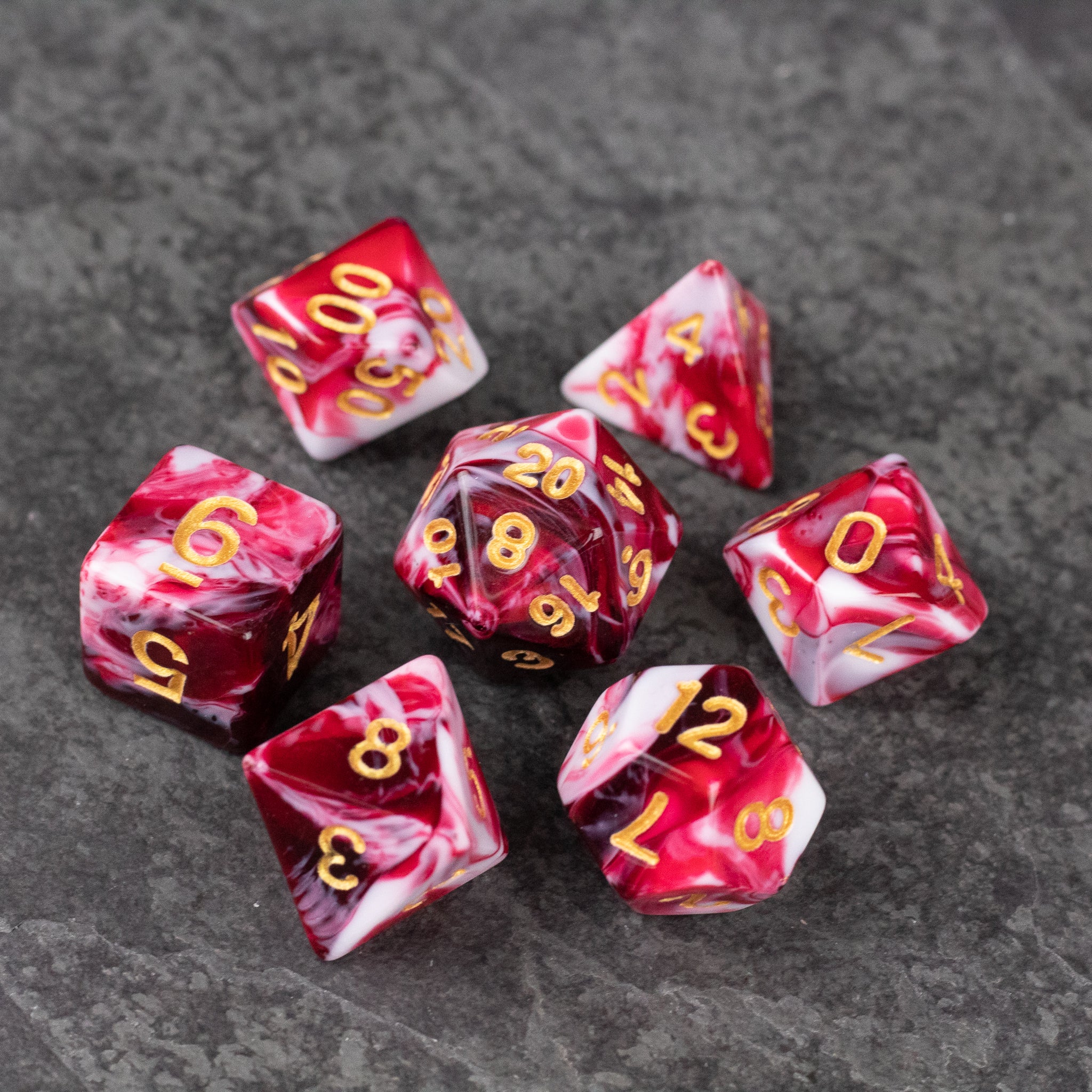 Red and White Marbled Dice Set - Set of seven acrylic dice with red and white marbled patterns and gold numbering on a dark surface.