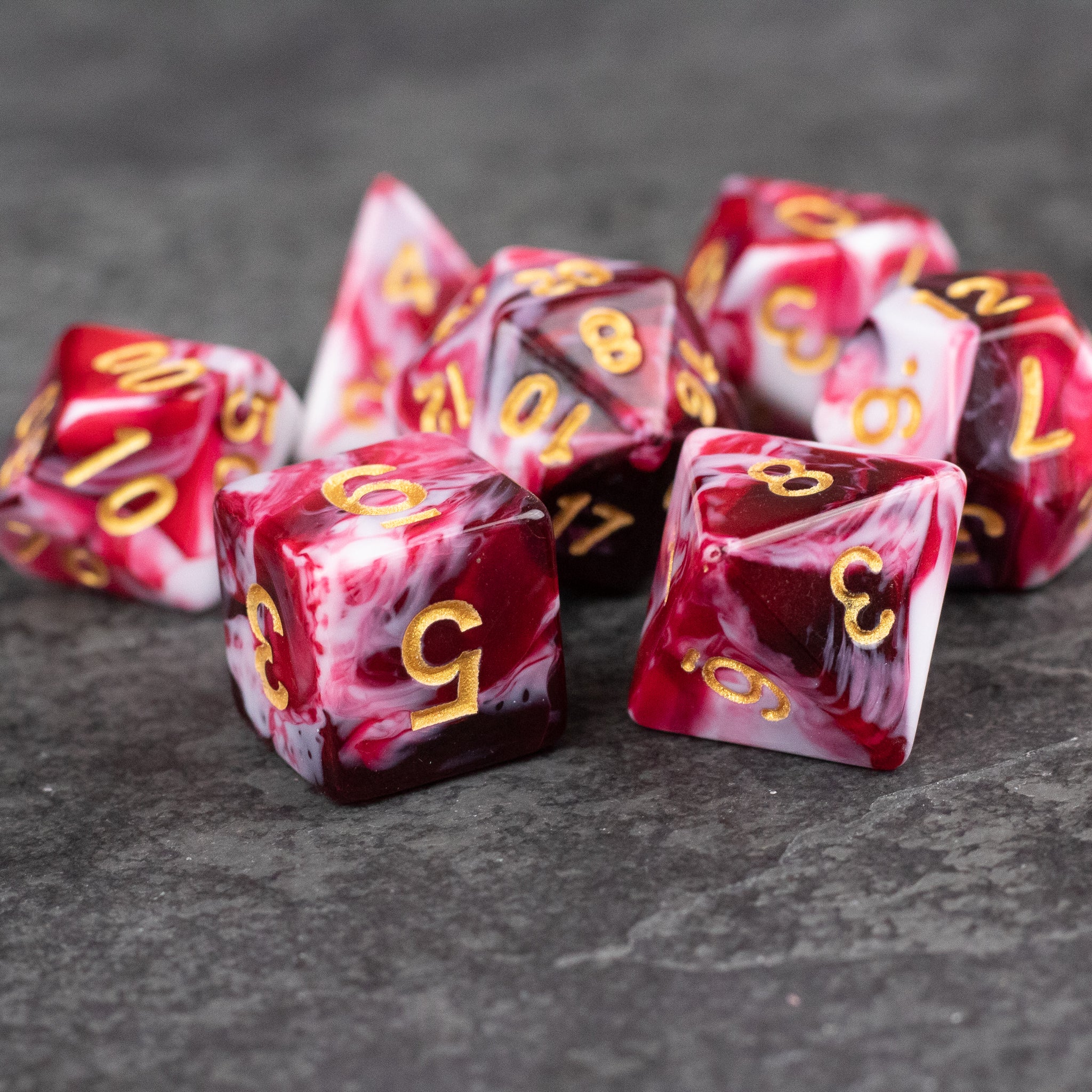 Red and White Marbled Dice Set - Set of seven red and white marbled acrylic dice with gold numbers on a dark surface.