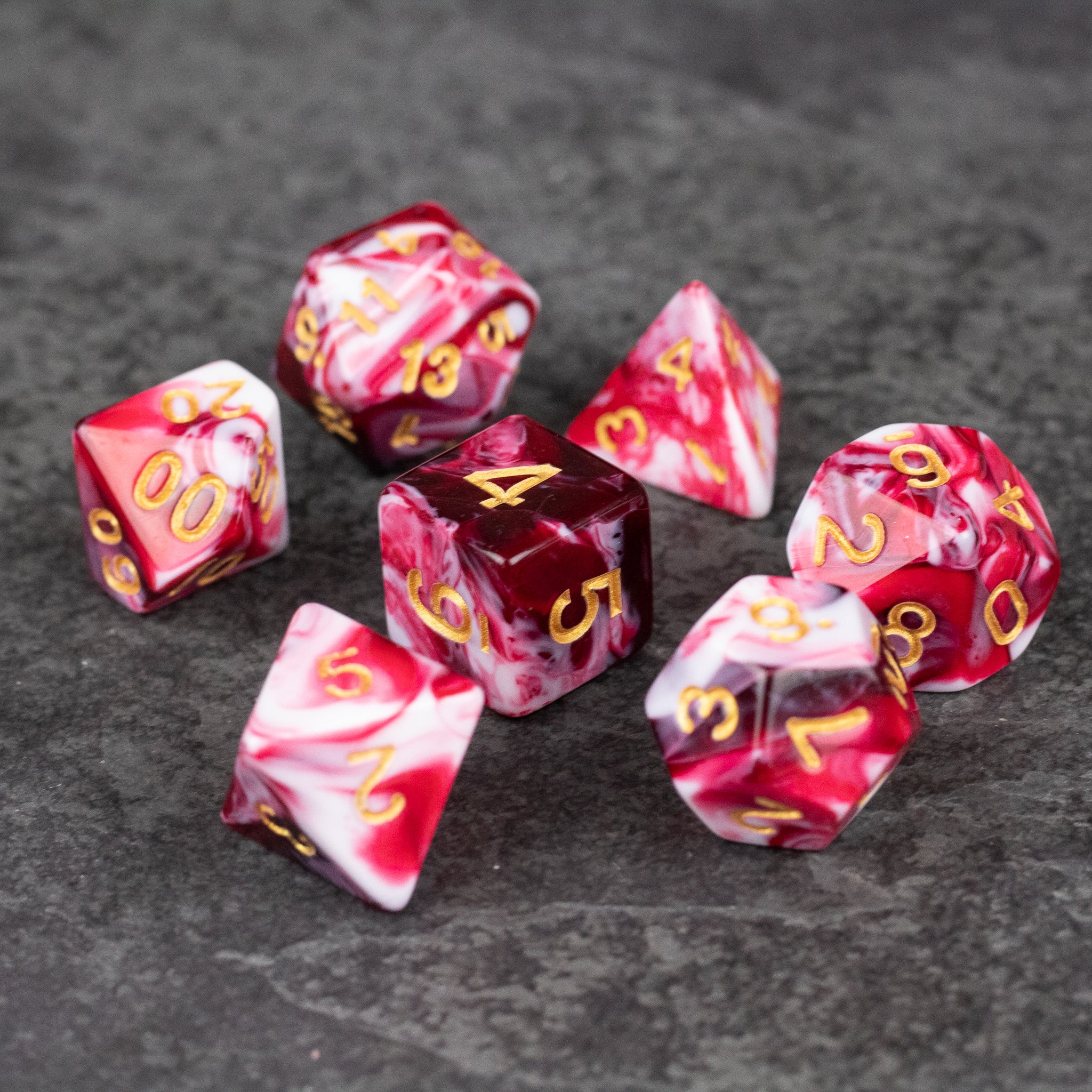 Red and White Marbled Dice Set - Red and white marbled acrylic dice set with gold numbering, includes various polyhedral shapes.