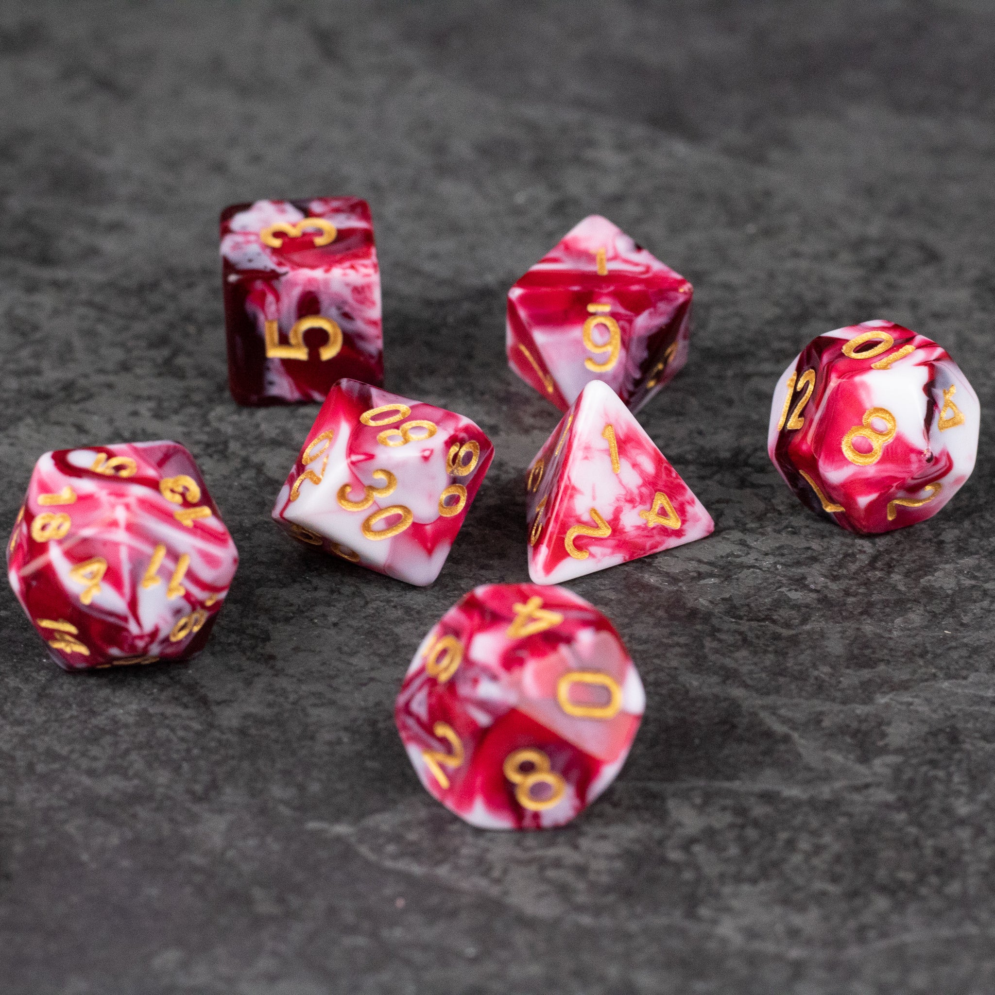 Red and White Marbled Dice Set - Seven-piece acrylic dice set with red and white marbled pattern and gold numbering.