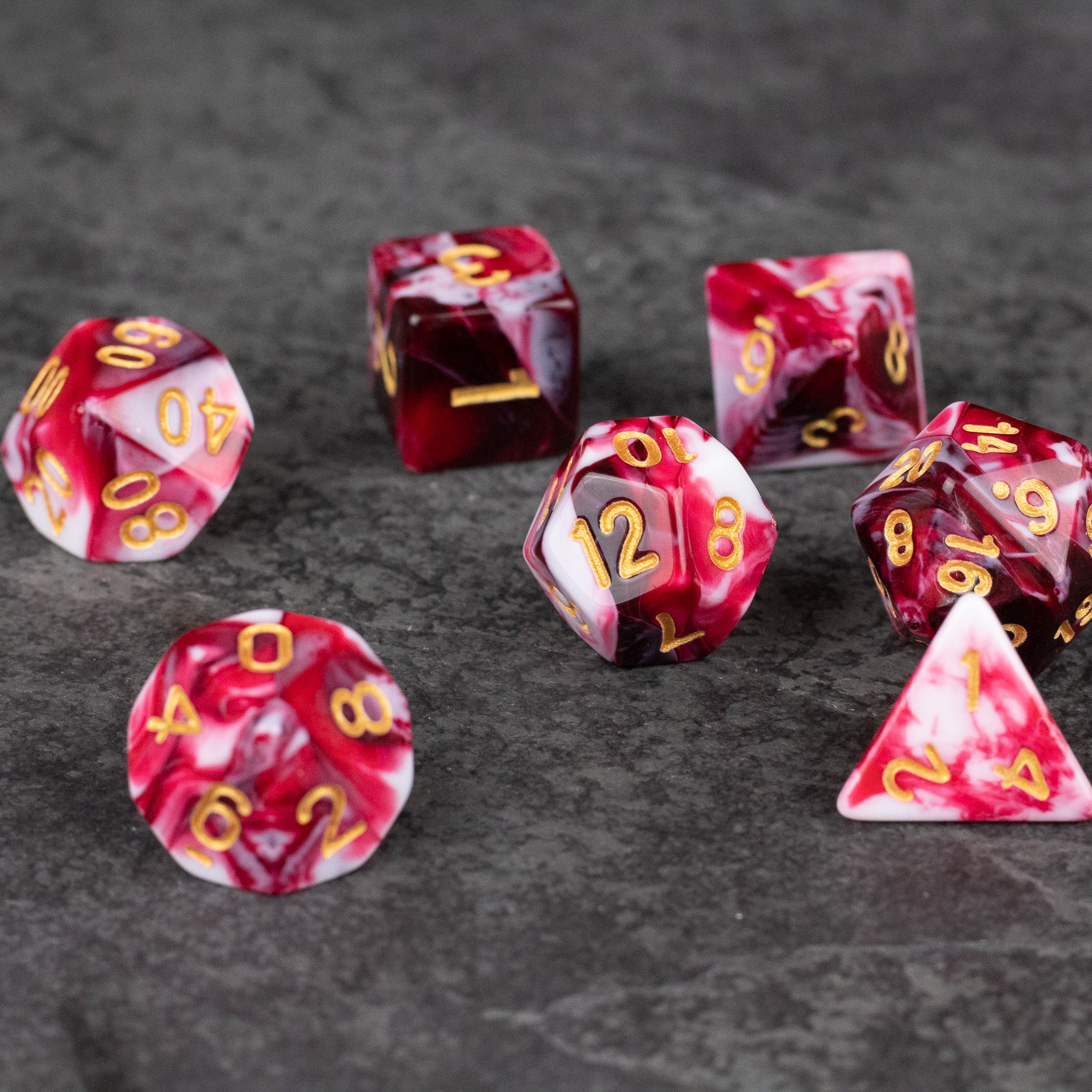Red and White Marbled Dice Set - Set of seven red and white marbled acrylic dice with gold numbering on a gray surface.