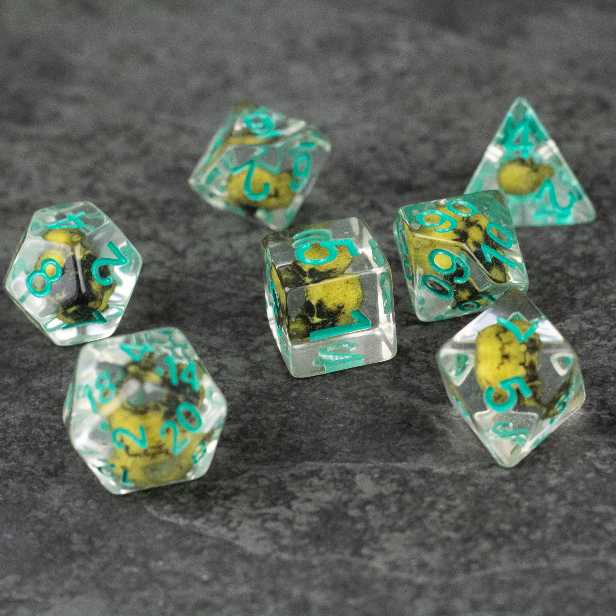 Yellow Skull Dice Set - Transparent yellow polyhedral dice set with green numbers and embedded skull designs on a gray surface.