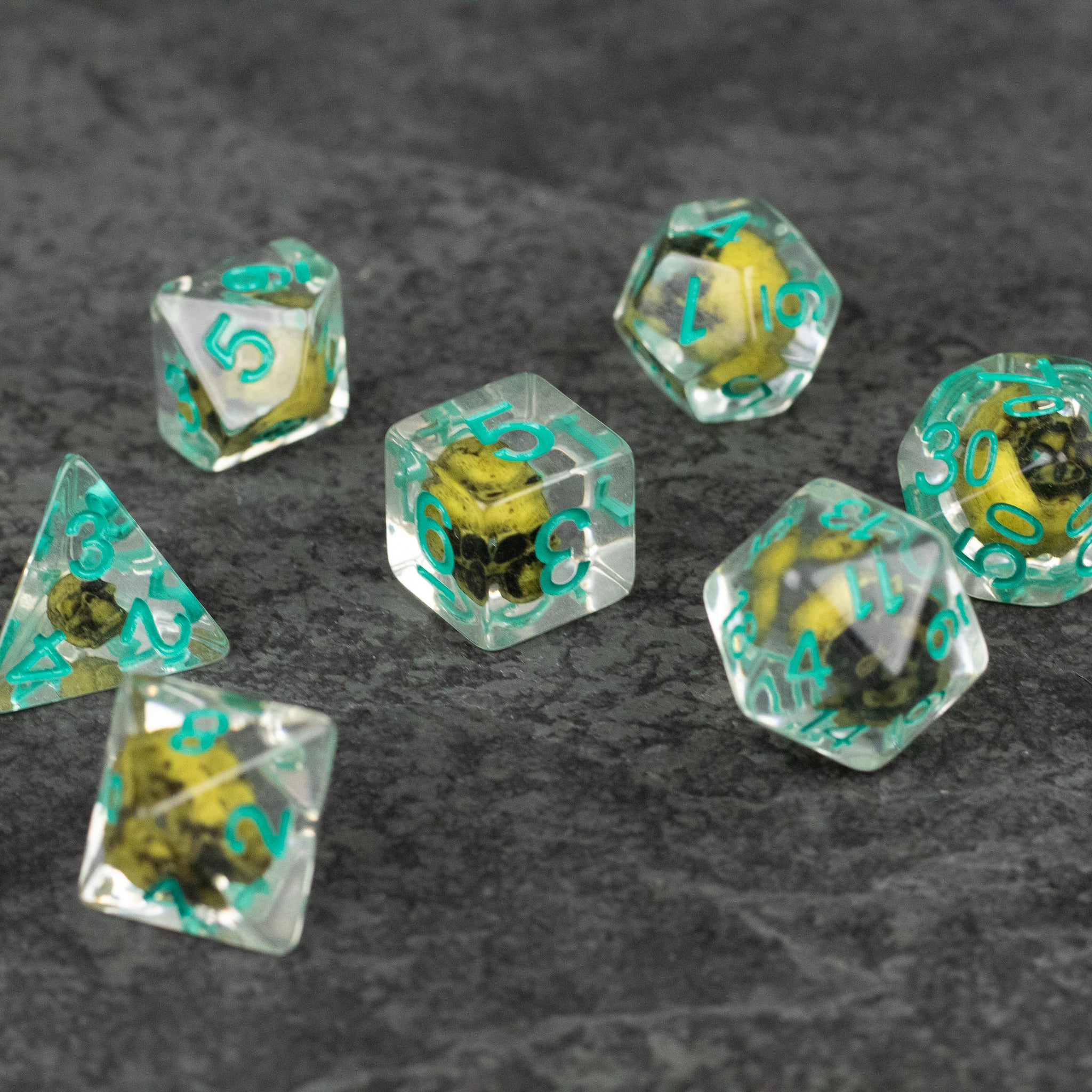 Yellow Skull Dice Set - Set of translucent polyhedral dice with yellow skulls inside and teal numbers, for tabletop games.