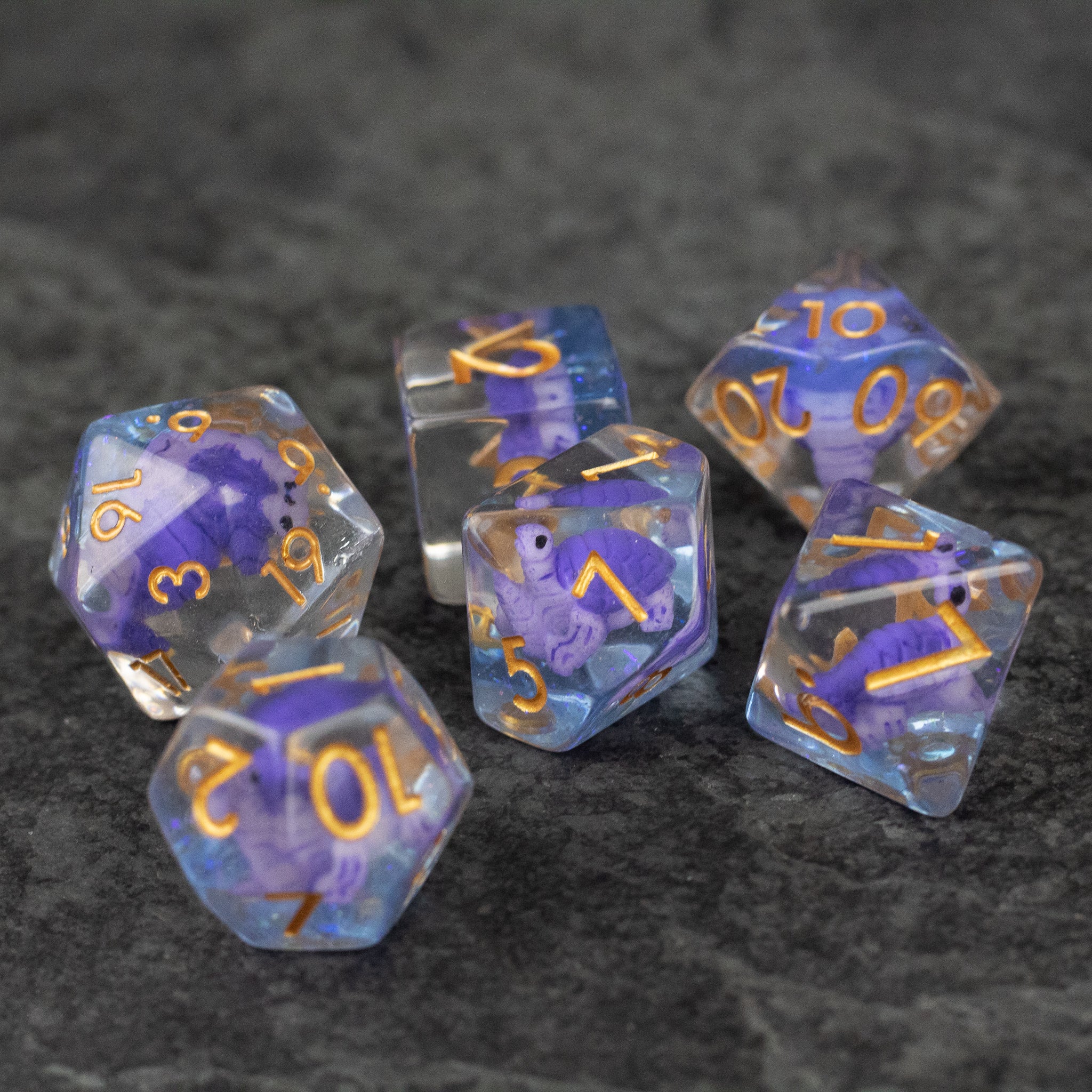 Purple Turtle Dice Set - Set of six clear dice with purple turtle inclusions and gold numbers on dark gray background.