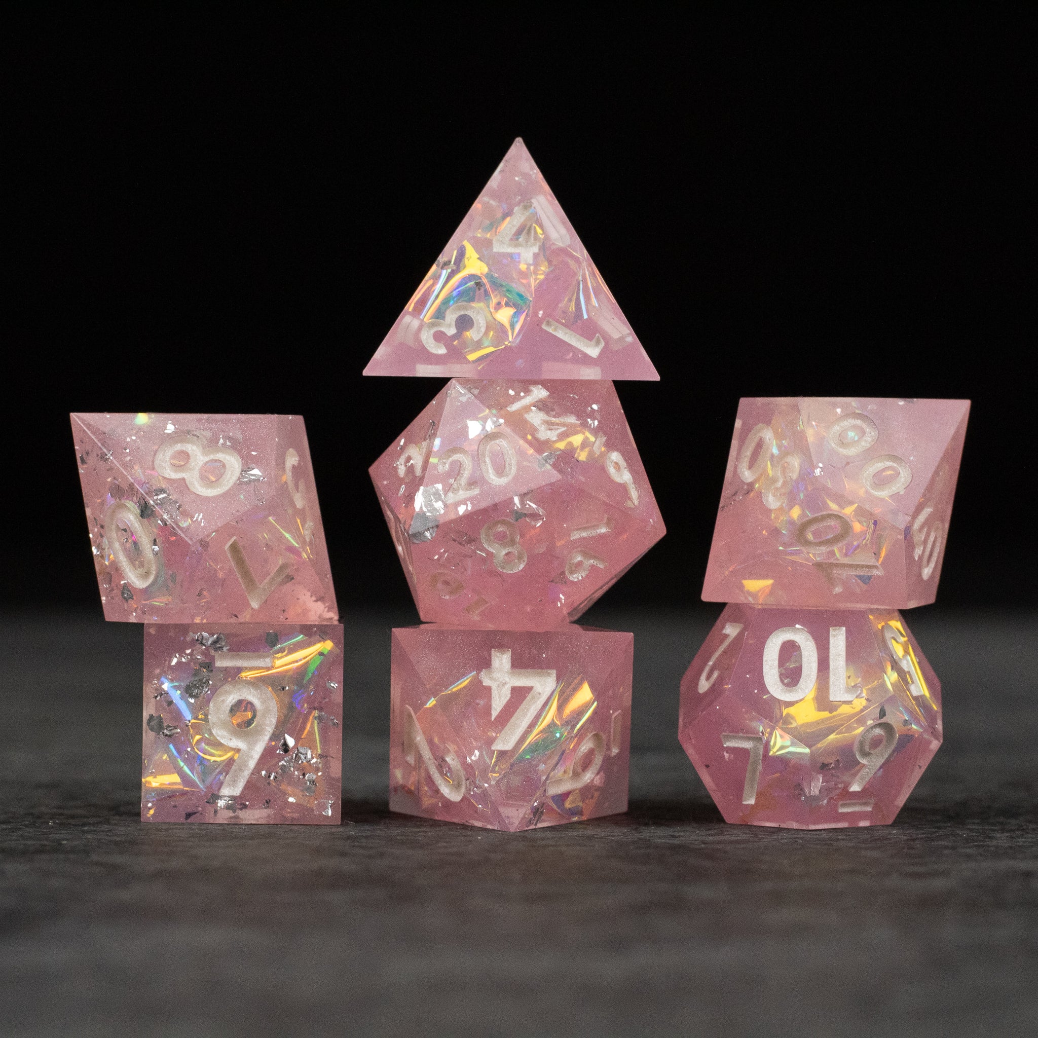 Bubblegum Dice Set - Pink translucent sharp edge dice set with colorful iridescent flakes and white numbers, seven pieces.