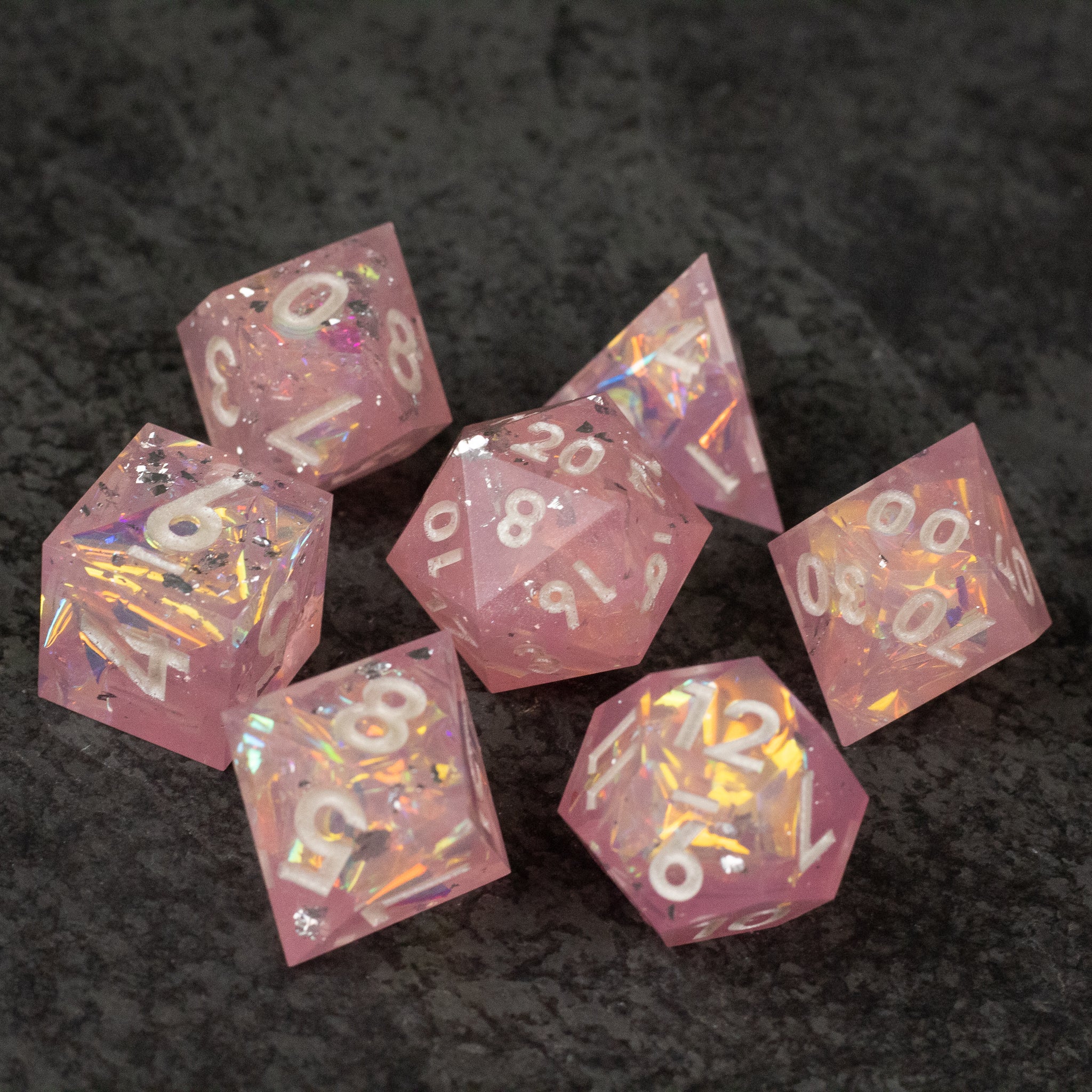 Bubblegum Dice Set - Set of seven translucent pink sharp-edged dice with gold numbers on a dark surface.