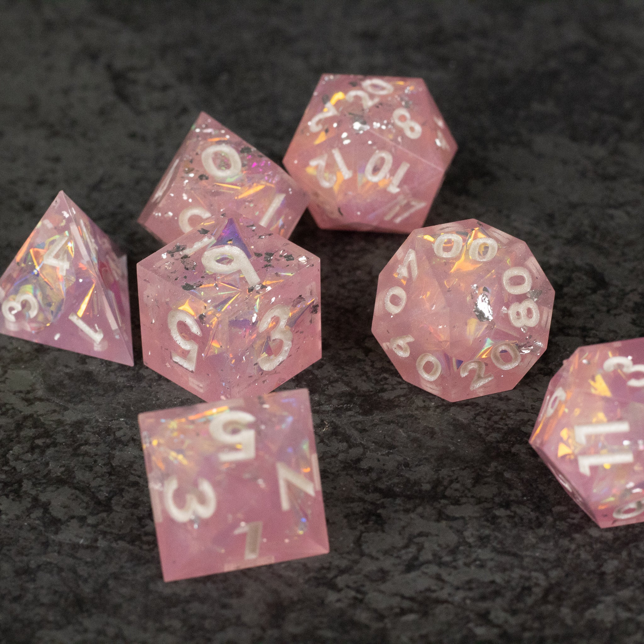 Bubblegum Dice Set - Set of seven pink sharp-edged polyhedral dice with white and gold numbering on dark textured background.