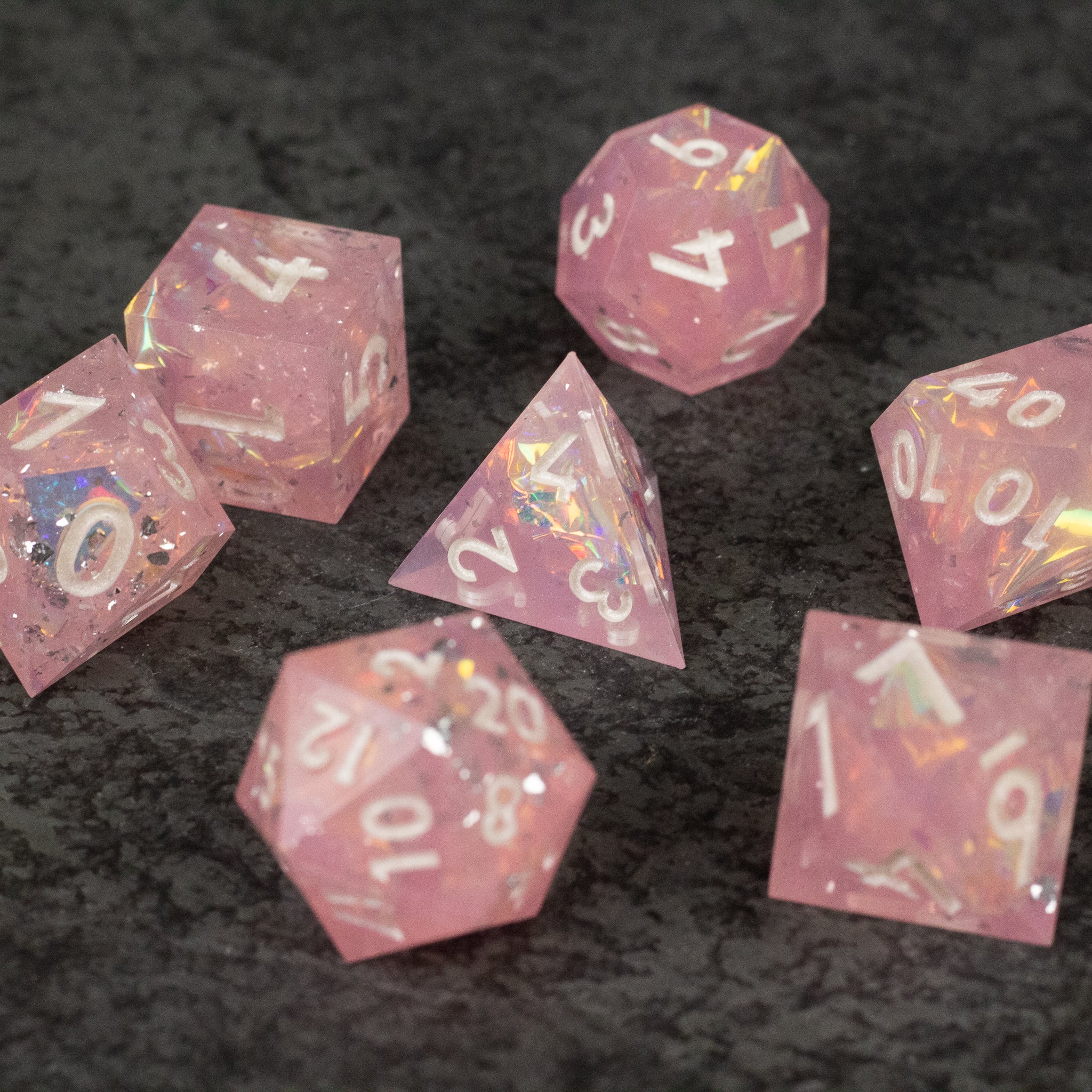 Bubblegum Dice Set - Translucent pink sharp-edged polyhedral dice set with white and gold numbering on a dark surface.