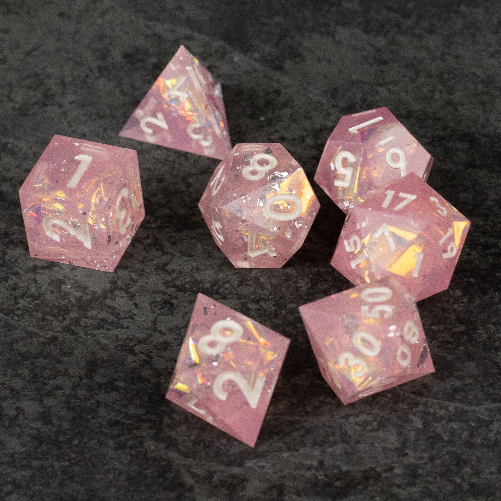 Bubblegum Dice Set - Translucent pink sharp-edged polyhedral dice set with gold numbering on black surface.