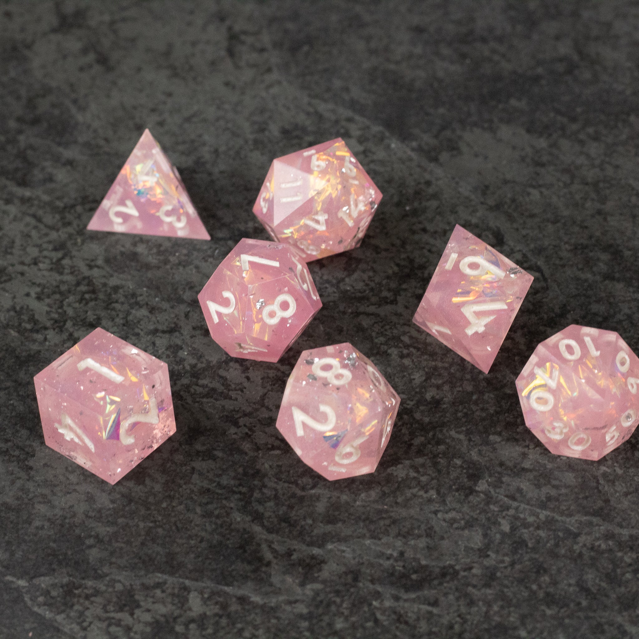 Bubblegum Dice Set - Set of seven pink translucent sharp-edged polyhedral dice with white numbers on a dark background.