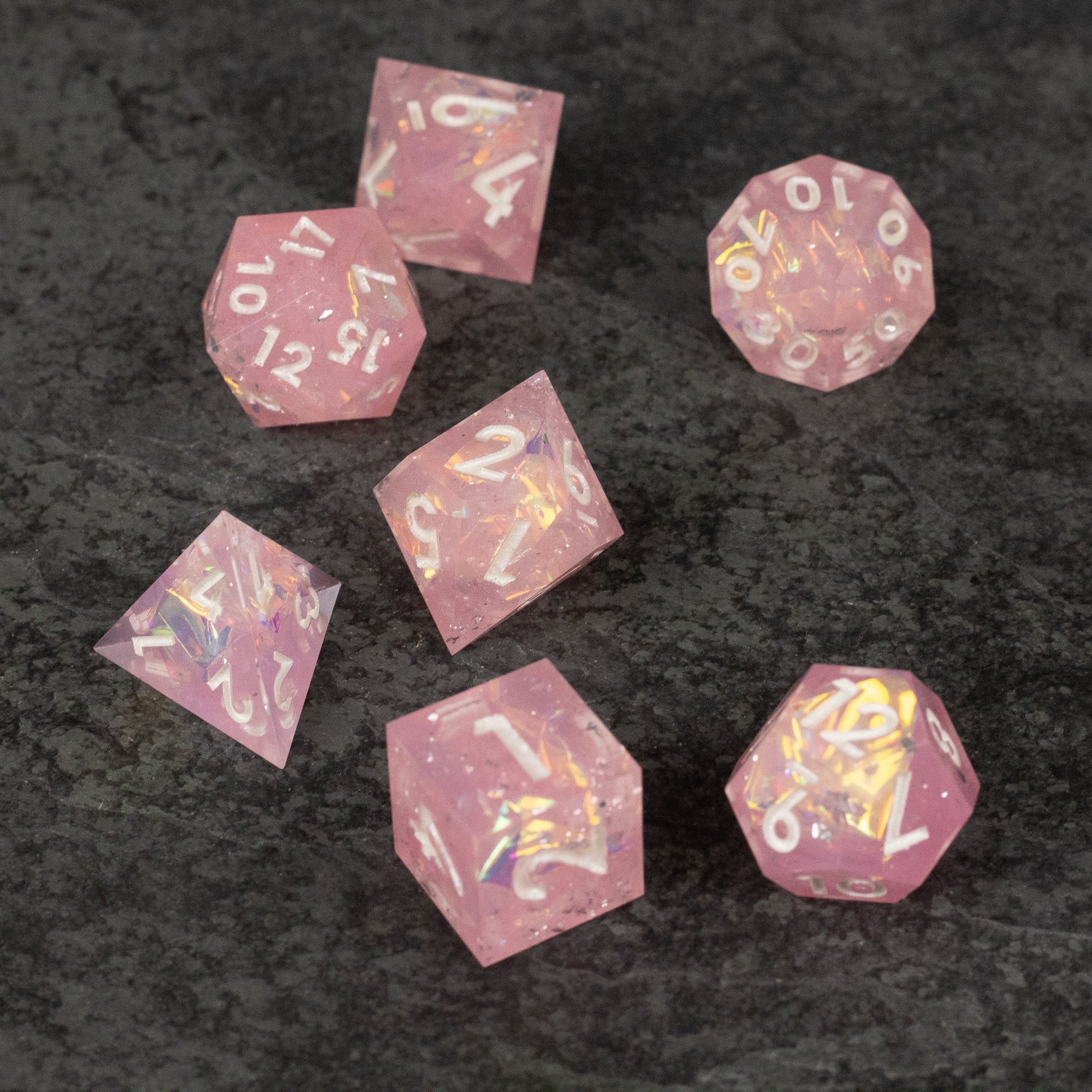 Bubblegum Dice Set - Seven sharp-edged translucent pink dice with white and gold numbering on a dark textured surface.
