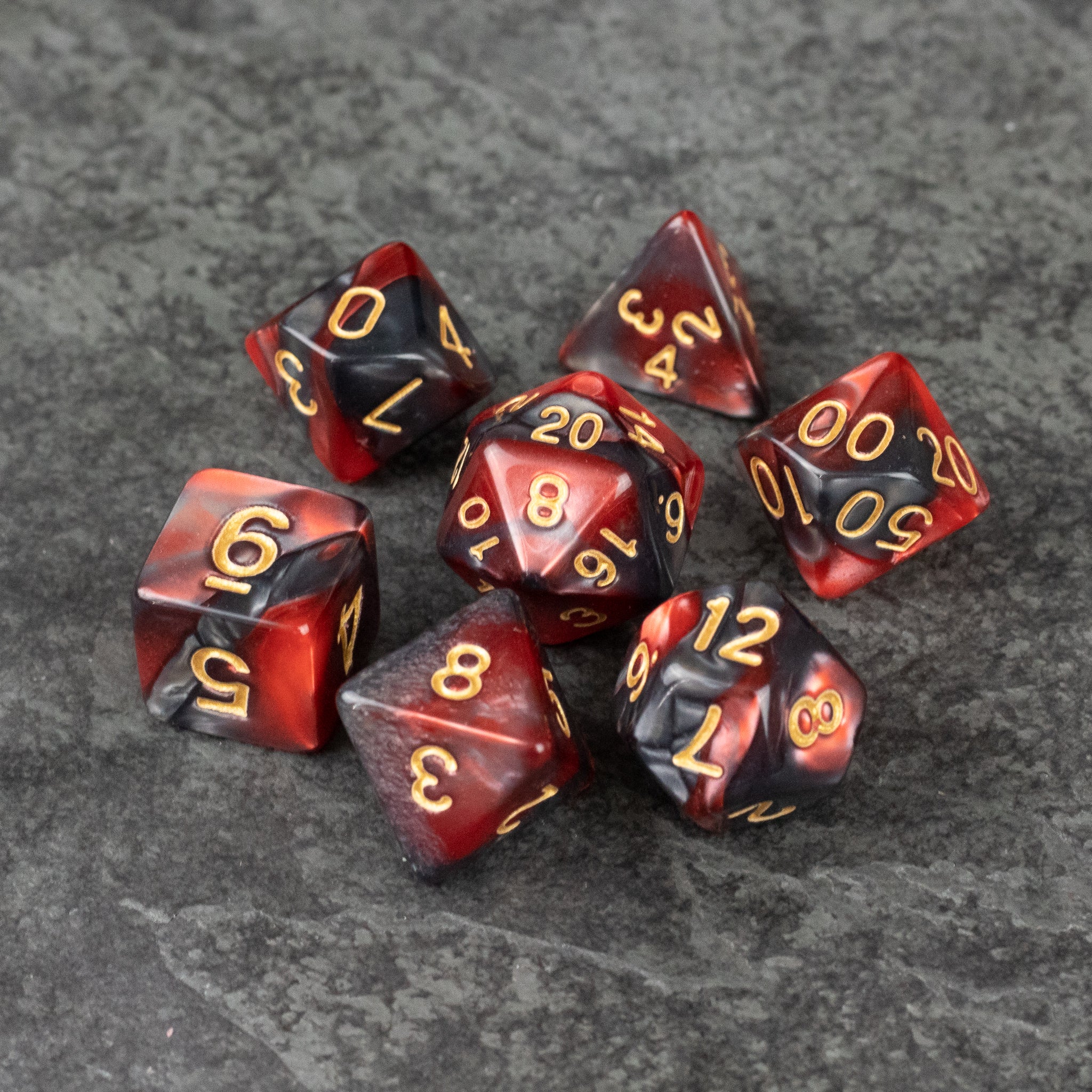Red and Black Marbled Dice Set - Set of seven red and black marbled acrylic dice with gold numbers on gray stone background.