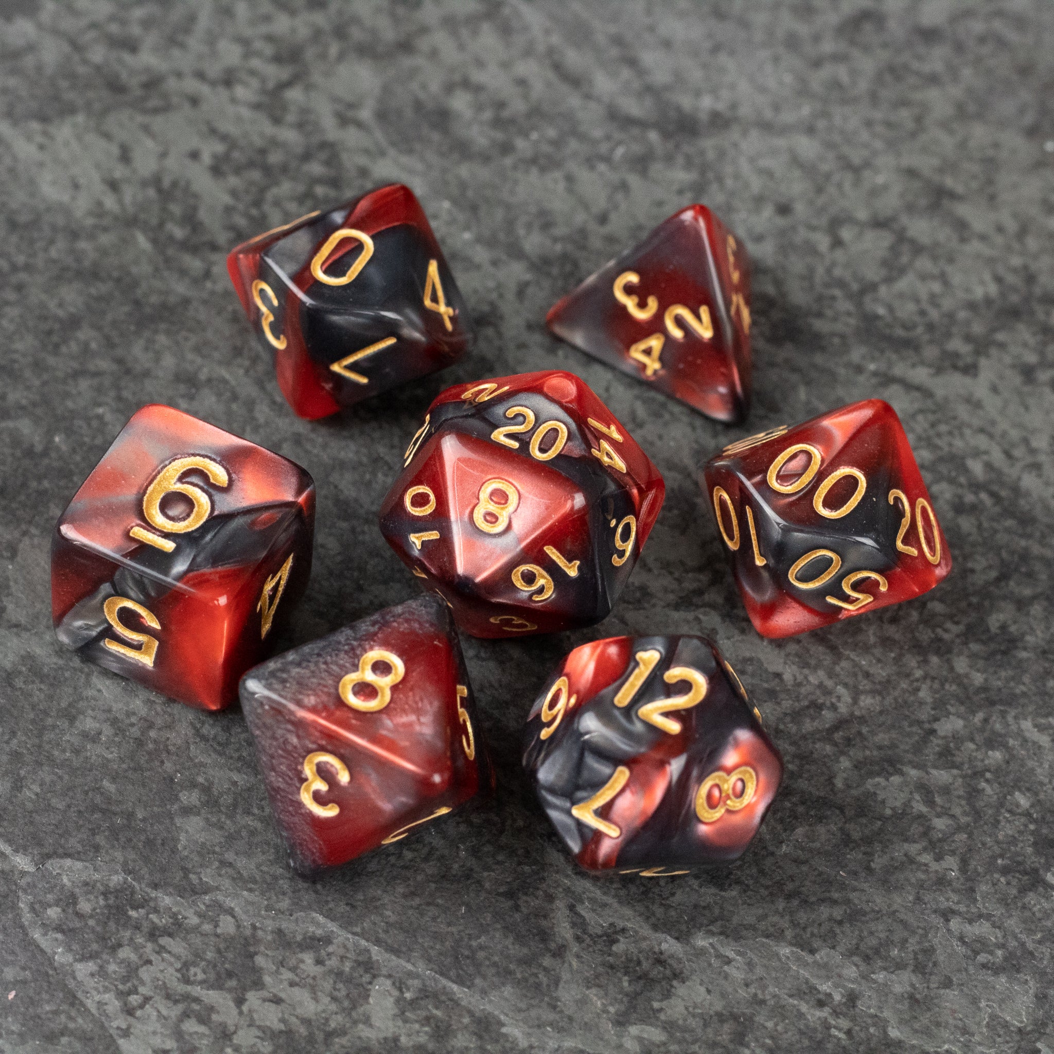 Red and Black Marbled Dice Set - Set of seven red and black marbled acrylic dice with gold numbering on dark stone surface.
