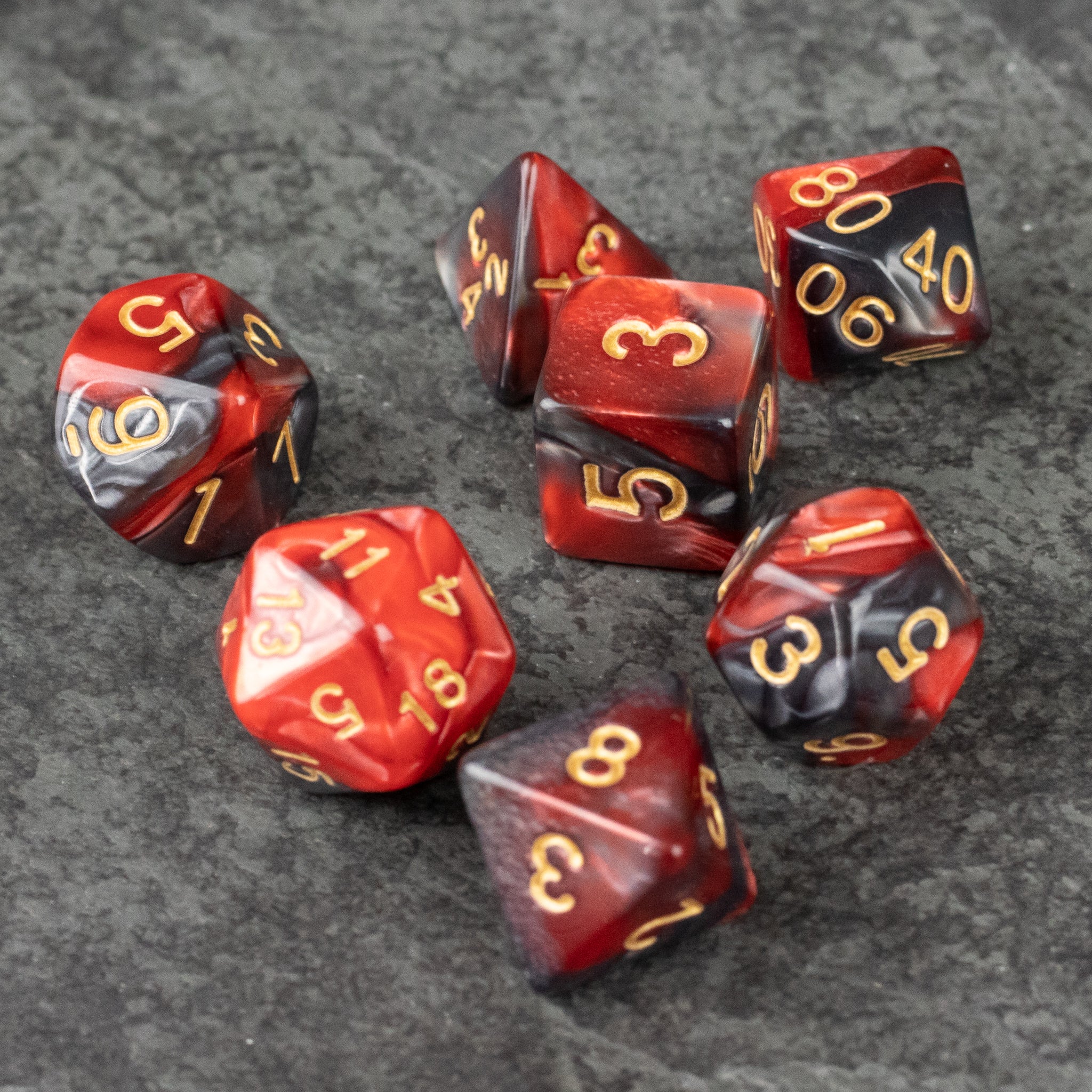 Red and Black Marbled Dice Set - Set of seven acrylic dice with red and black marbled pattern and gold numbering on gray surface.