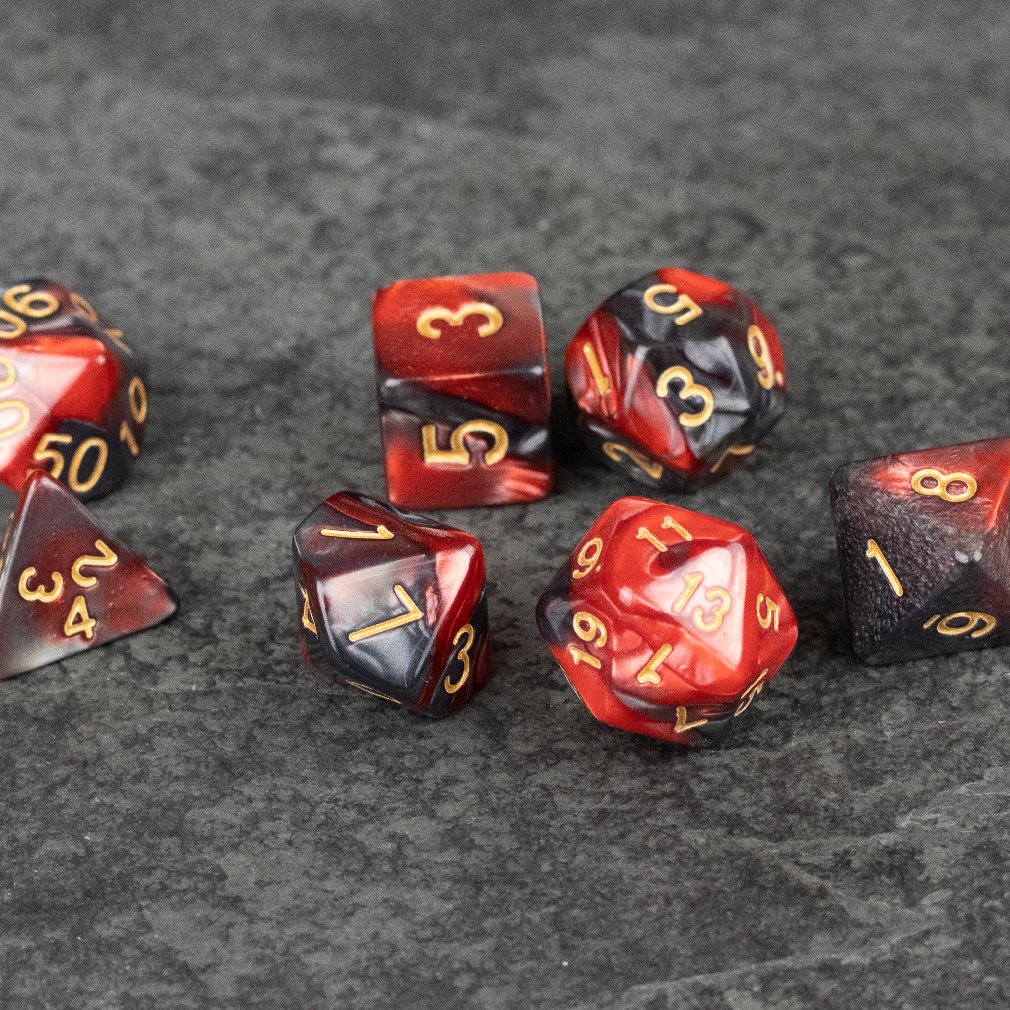 Red and Black Marbled Dice Set - Set of red and black marbled acrylic dice with gold numbering, featuring various polyhedral shapes.