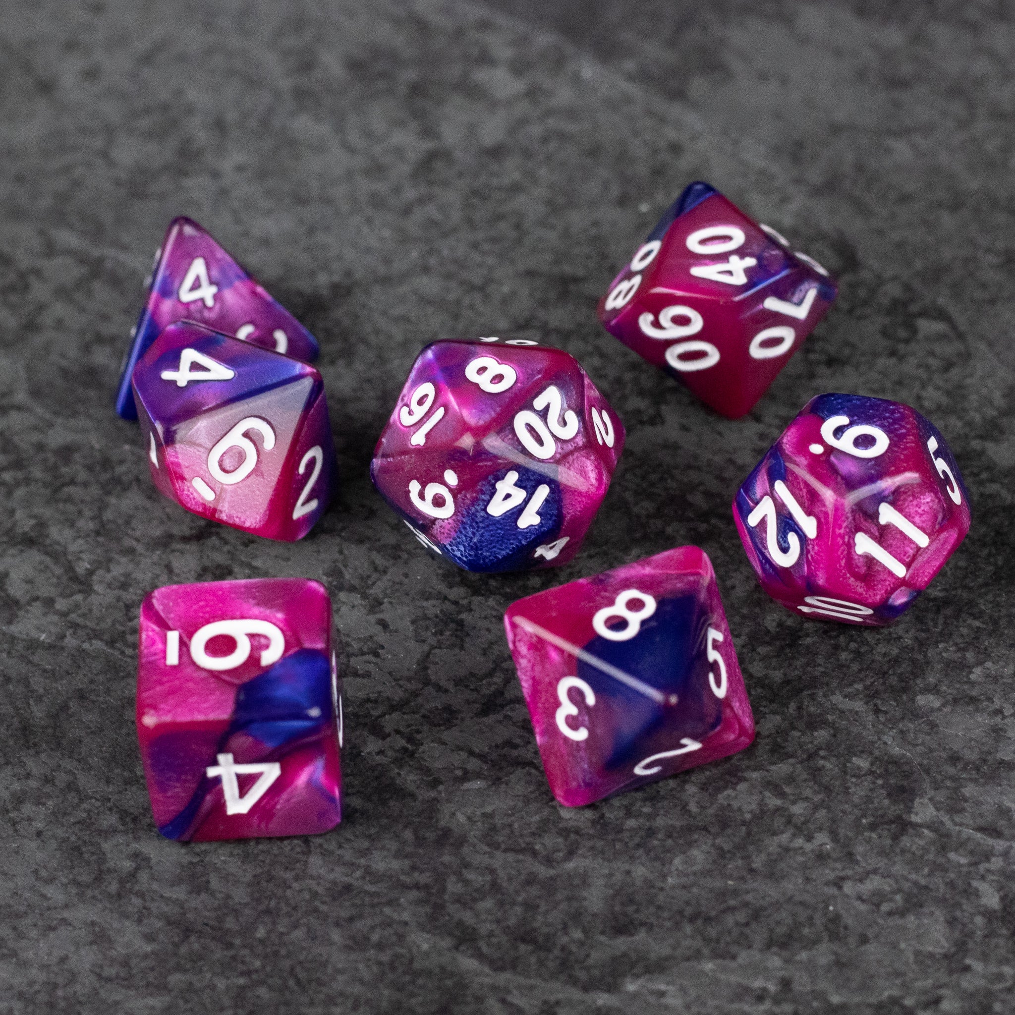 Pink and Blue Marbled Dice Set - Seven pink and blue marbled acrylic dice with white numbering on a gray surface.