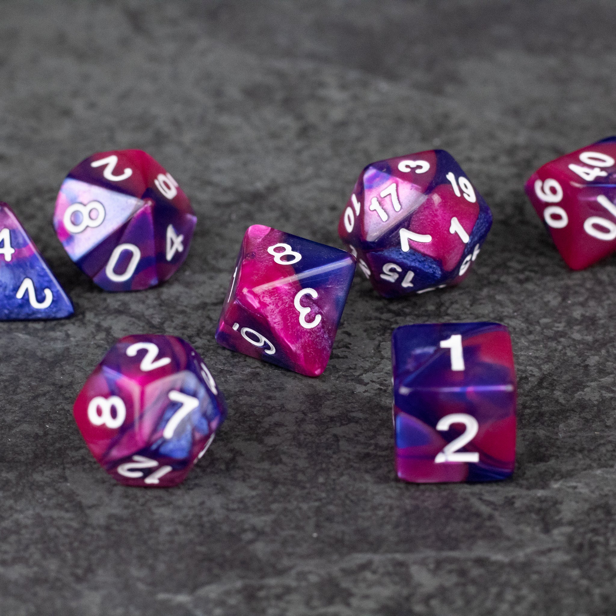 Pink and Blue Marbled Dice Set - Seven acrylic dice with pink and blue marbled patterns and white numbering.