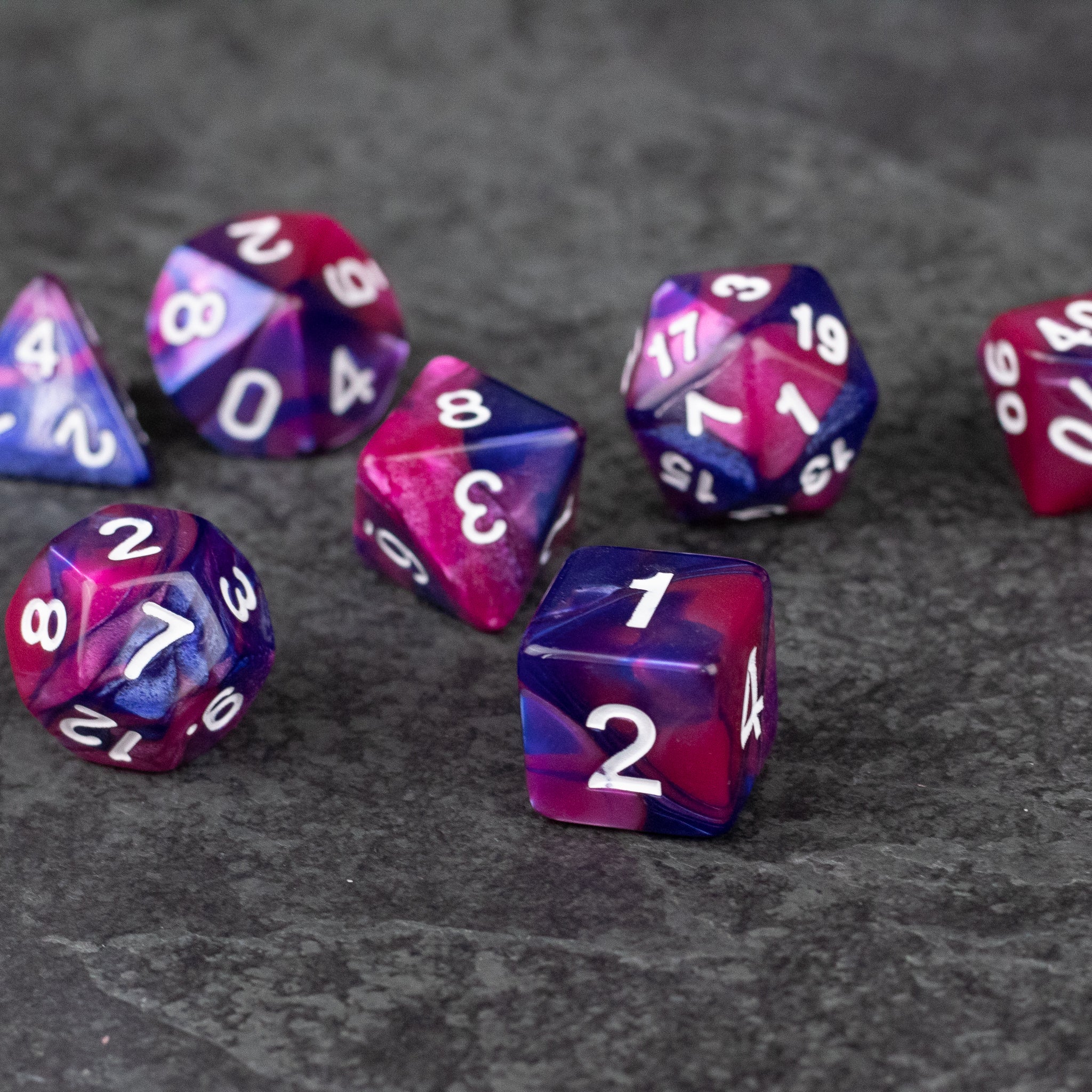 Pink and Blue Marbled Dice Set - Set of seven marbled acrylic dice in vibrant pink and blue with white numbering, including d4, d6, d8, d10, d12, and d20.