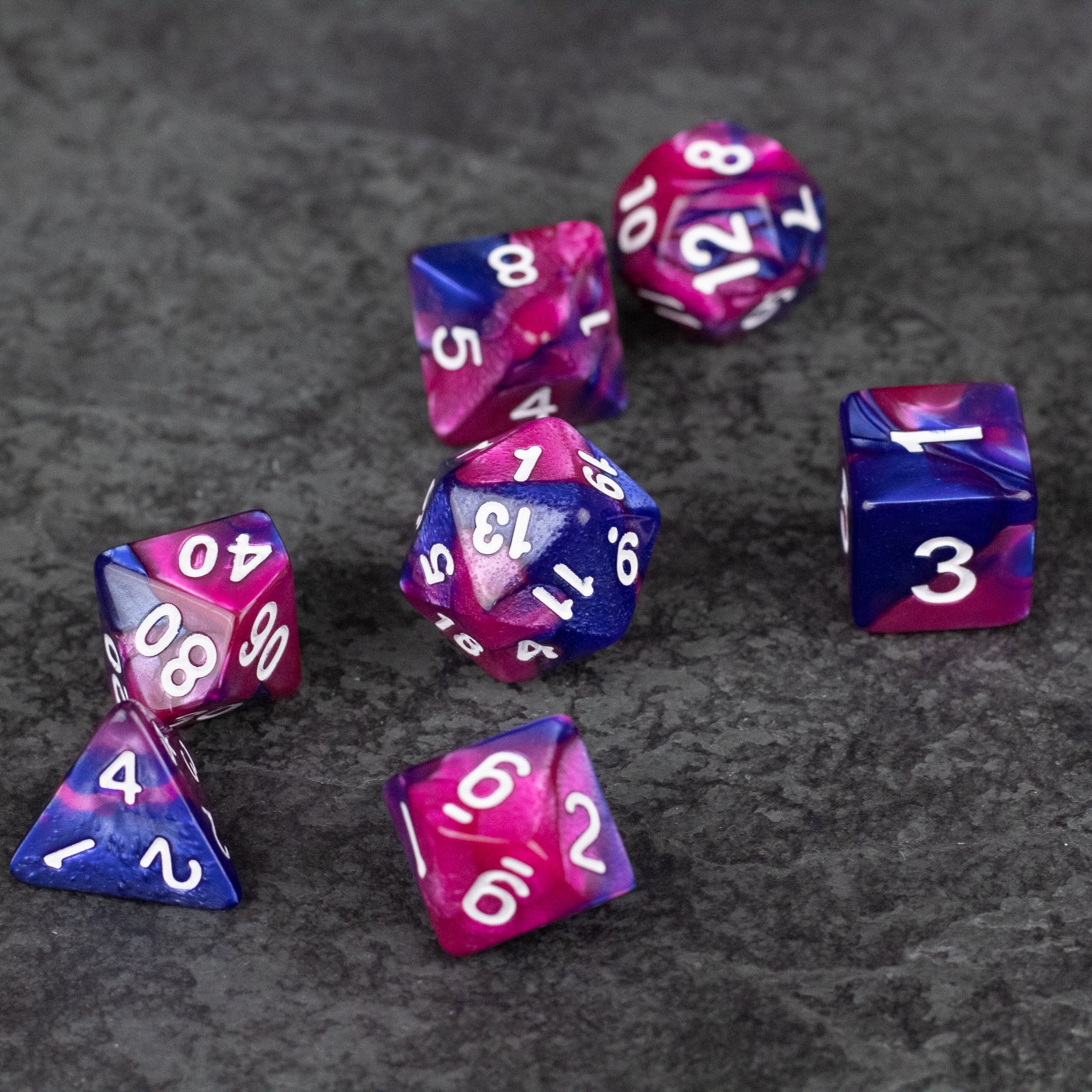 Pink and Blue Marbled Dice Set - Seven-piece set of pink and blue marbled acrylic dice with white numbering on a dark textured surface.