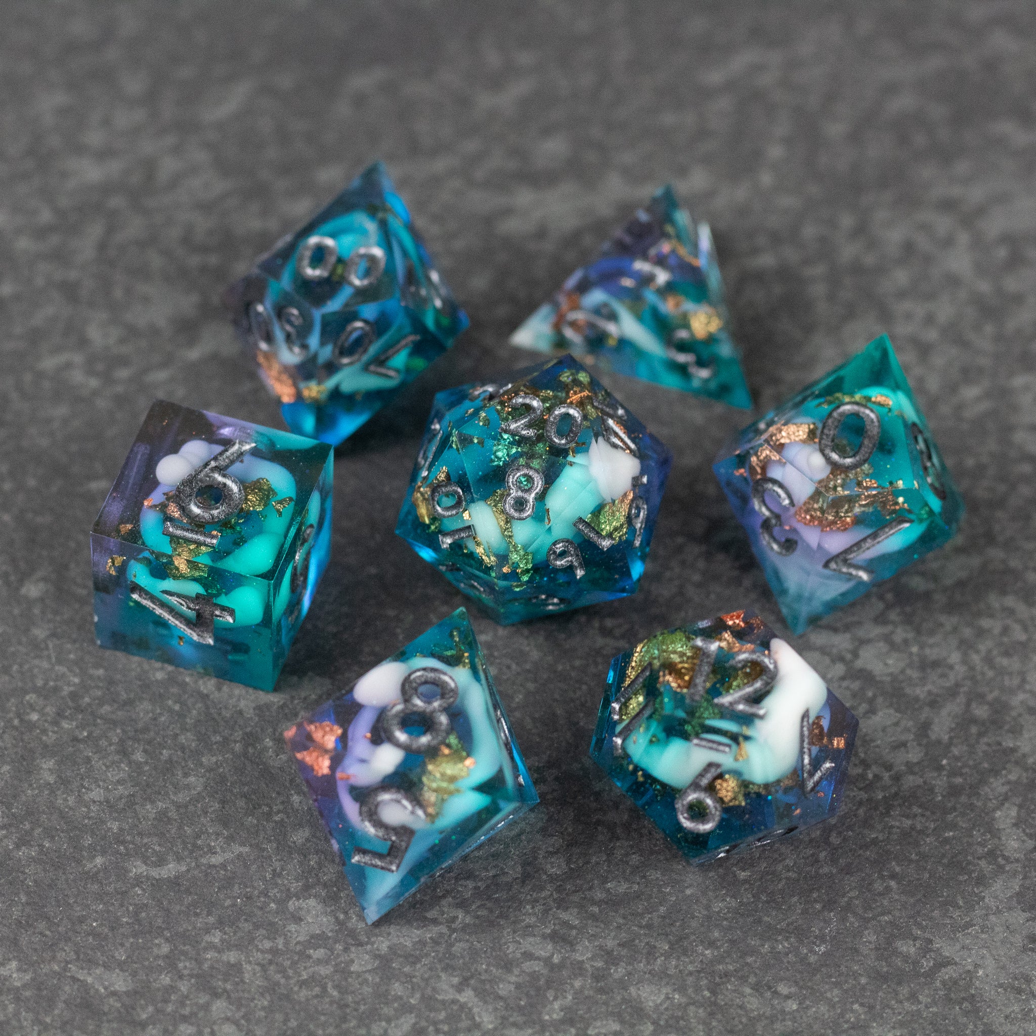 Frostfall Dice Set - Transparent blue and purple sharp edge dice set with gold numbering on gray stone surface.