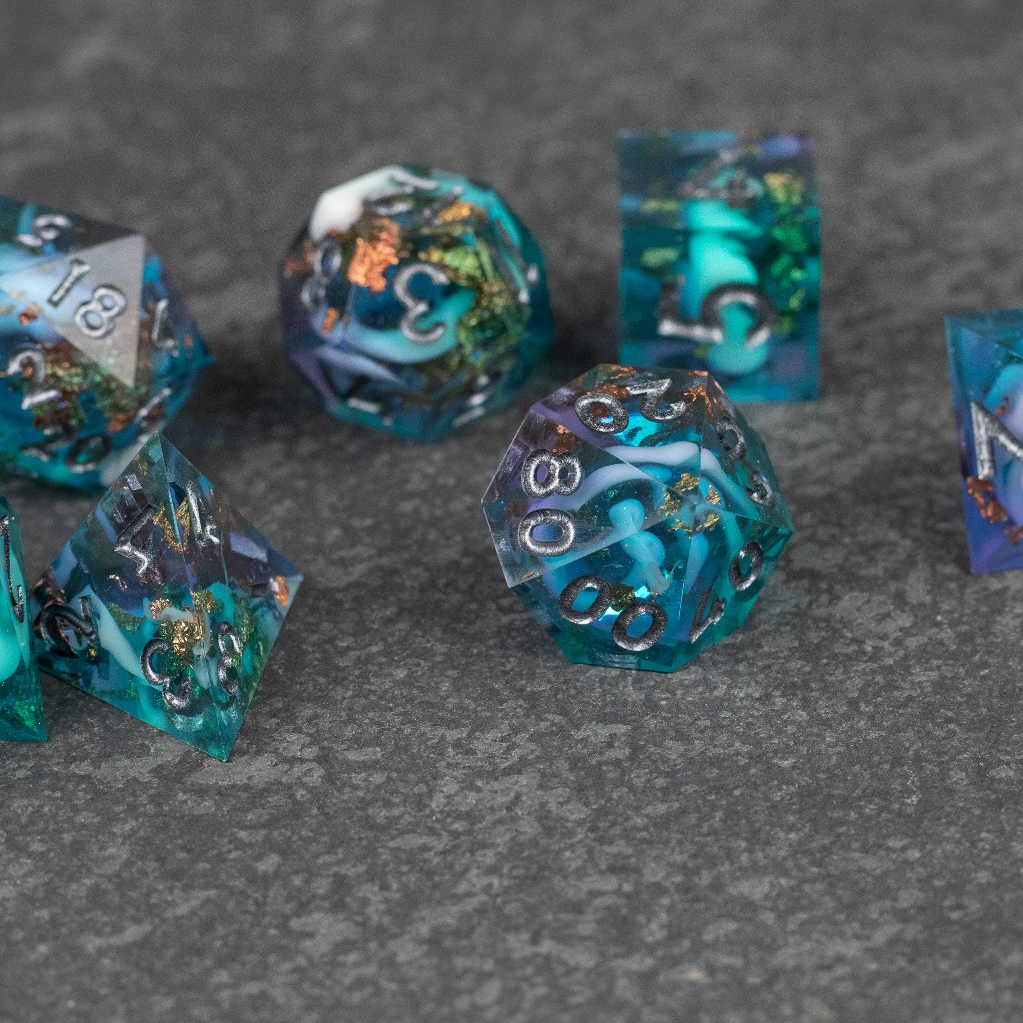 Frostfall Dice Set - Set of translucent blue polyhedral dice with sharp edges and white numbers on a gray stone surface.
