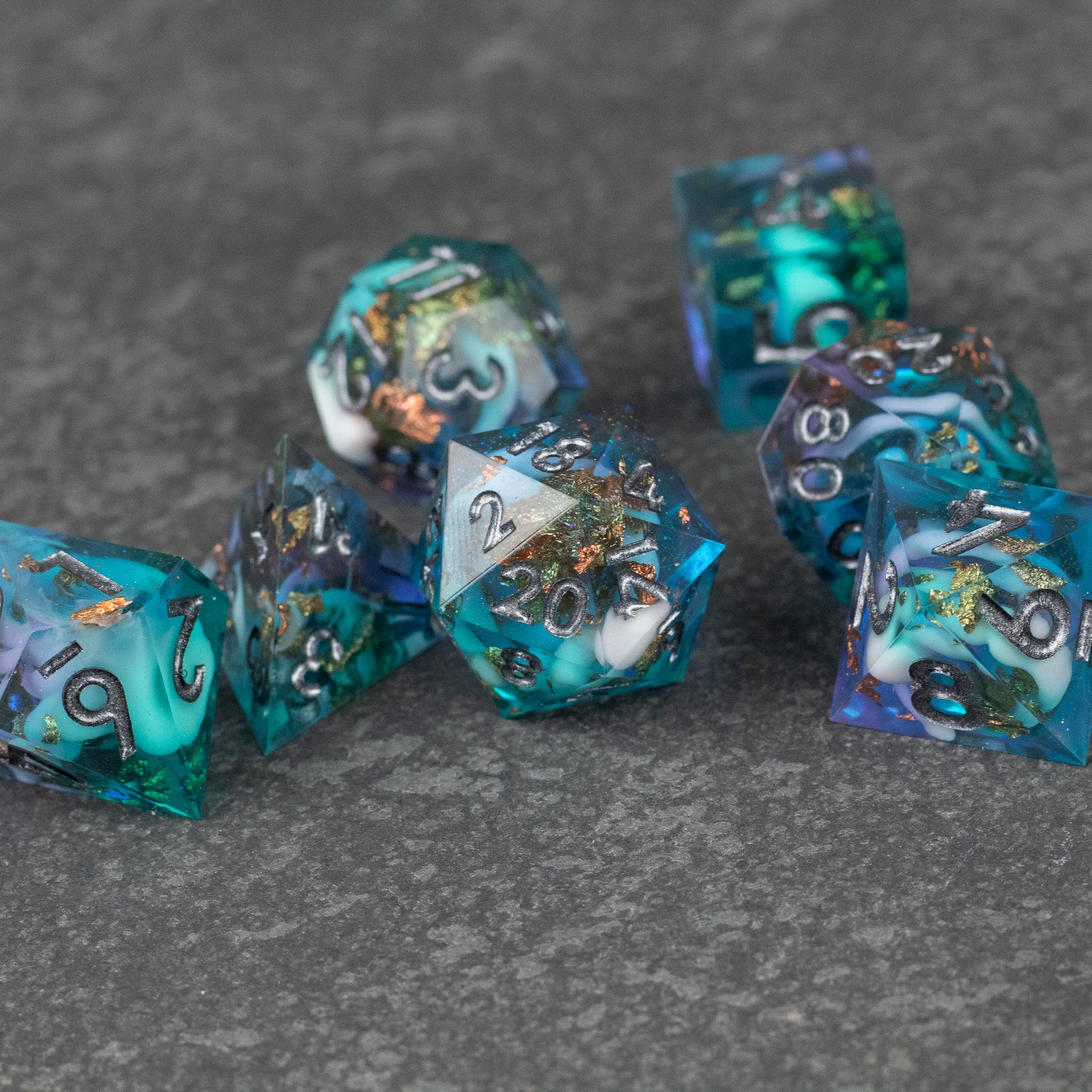 Frostfall Dice Set - Set of seven translucent polyhedral dice in blue and teal hues with silver numbers and sharp edges, featuring intricate.