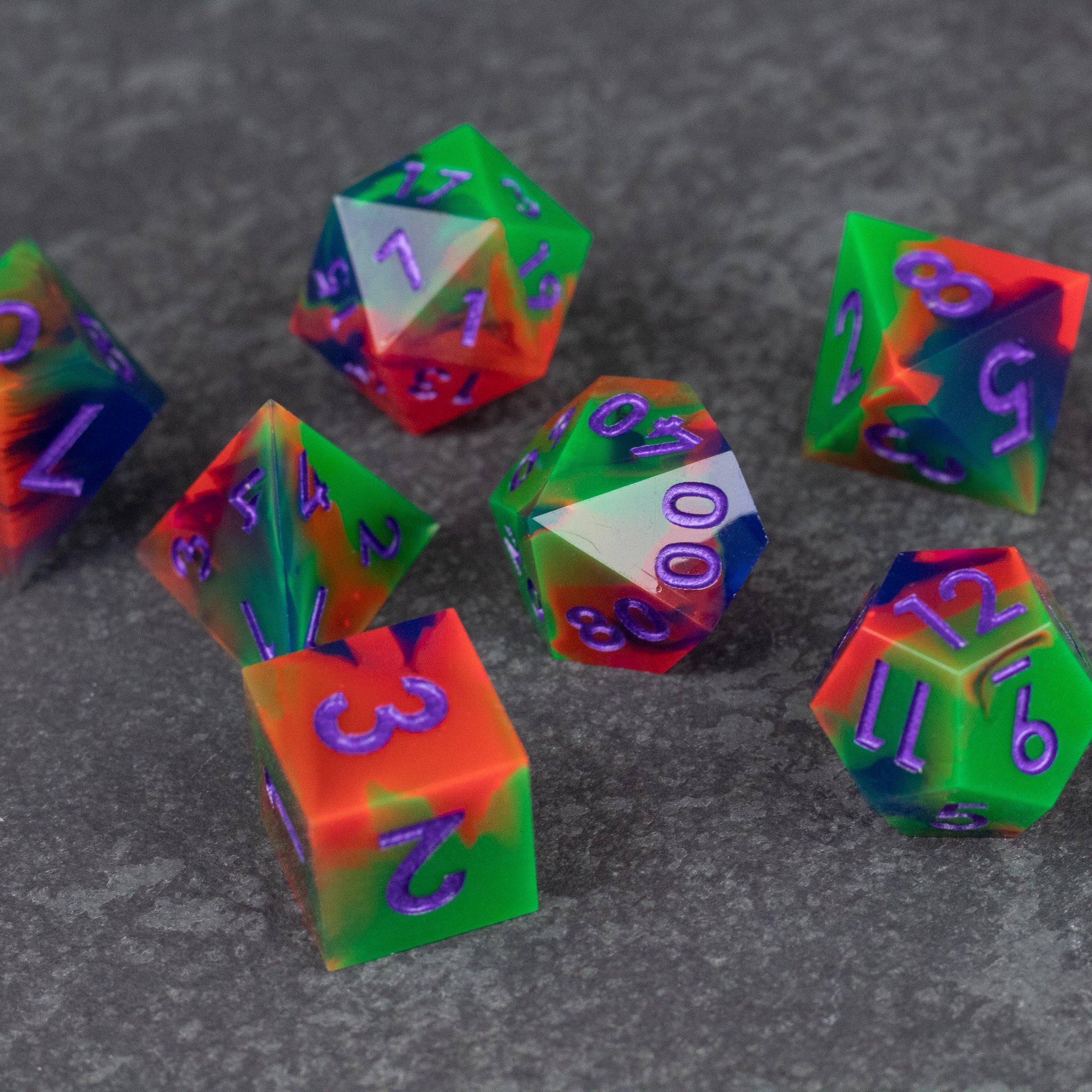 Neon Demon Dice Set - Set of seven sharp-edged polyhedral dice in translucent green, pink, and orange with neon purple numbers.