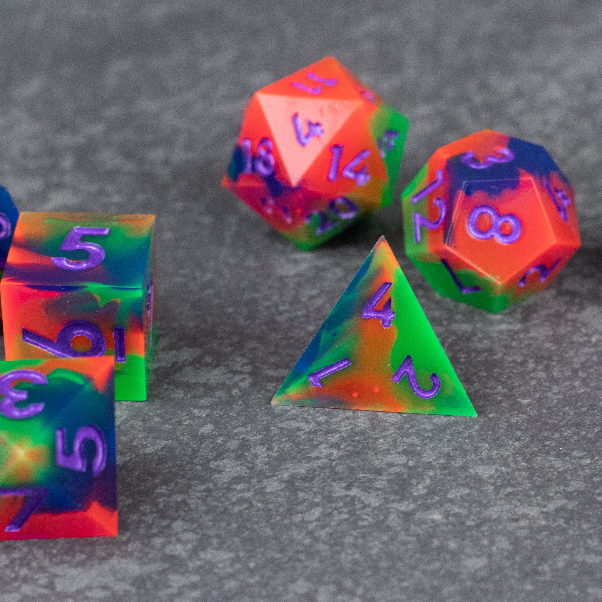Neon Demon Dice Set - Set of neon green and pink sharp-edged polyhedral dice with translucent material and purple numbers on a gray surface.