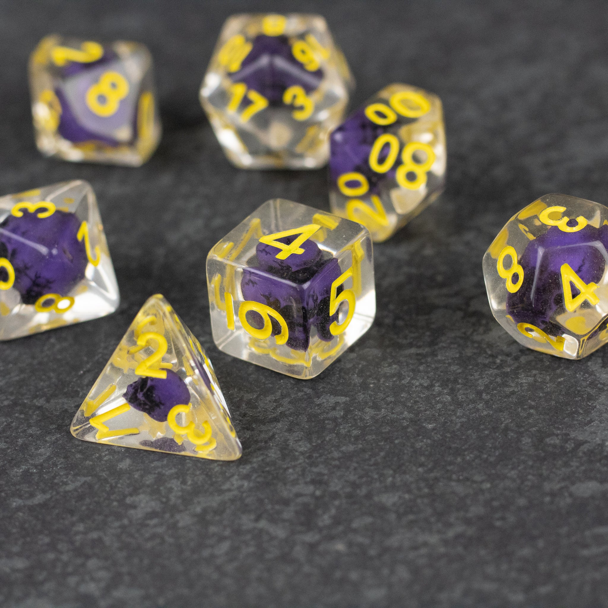 Purple Skull Dice Set - Transparent dice with embedded purple skulls and bright yellow numbers on a dark surface.